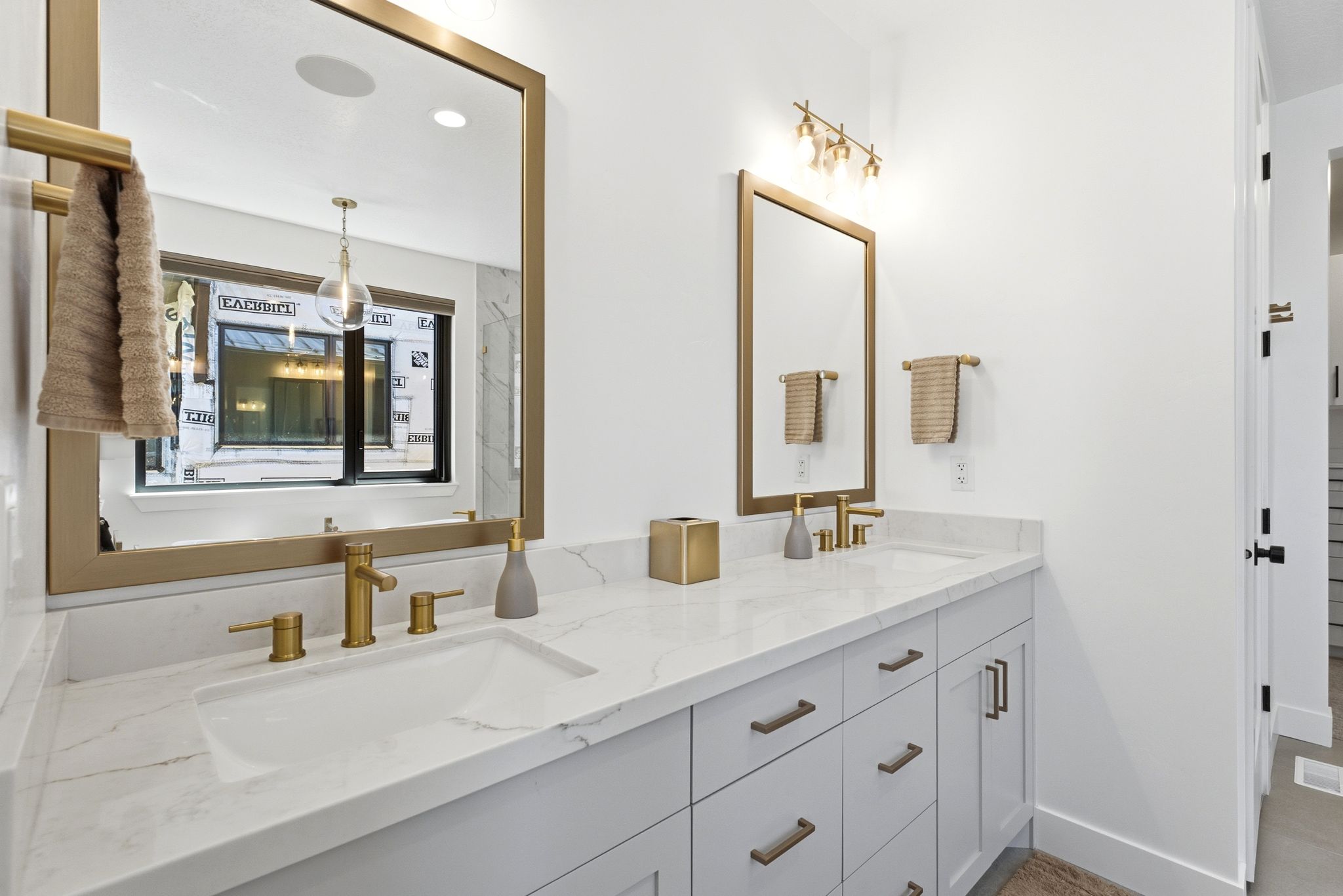 Dual vanity featuring white countertops with subtle veining, undermount sinks, and brass-finish hardware