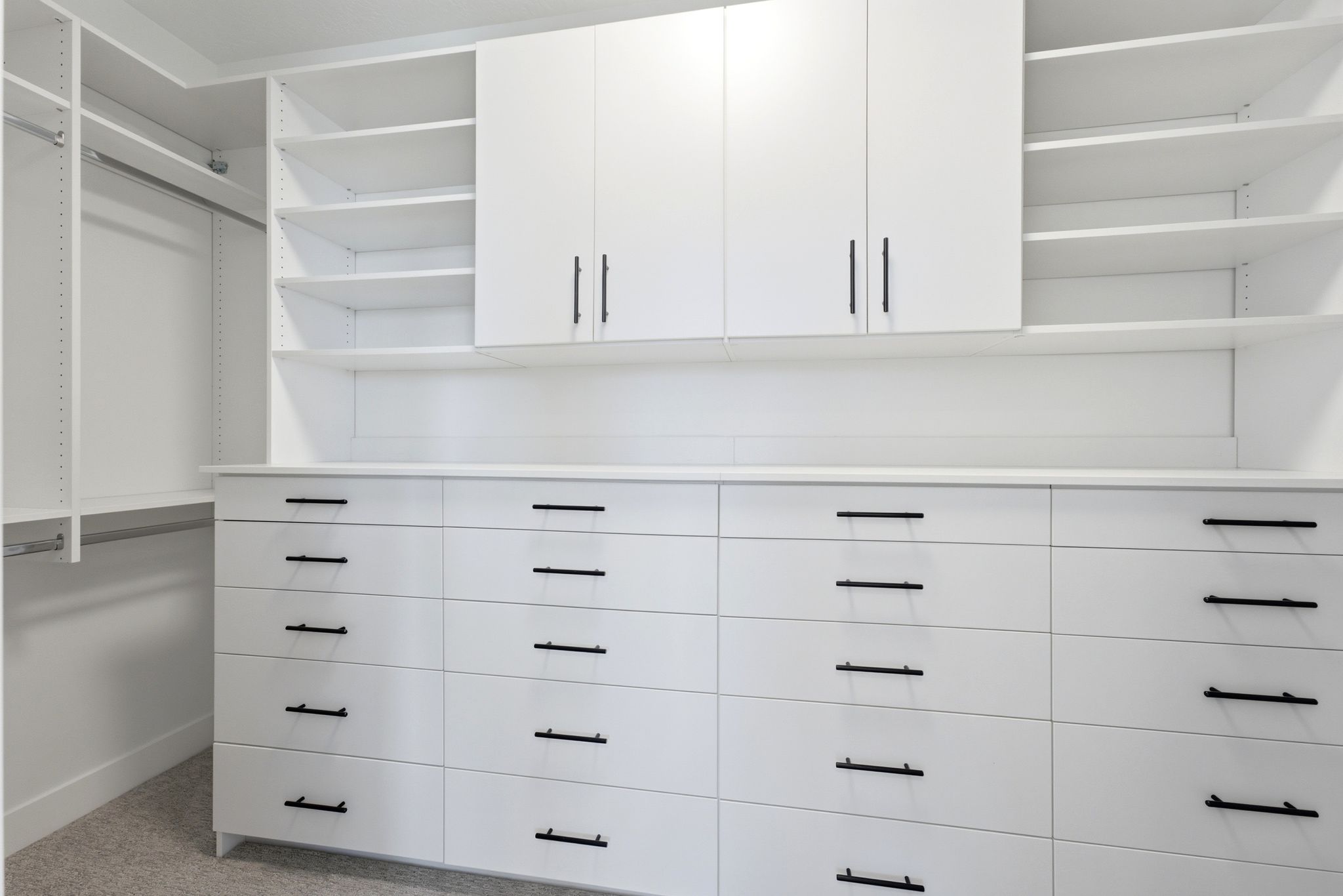 Integrated custom closet system featuring extensive white cabinetry, open shelving, multiple drawers with matte black pulls, and hanging rods