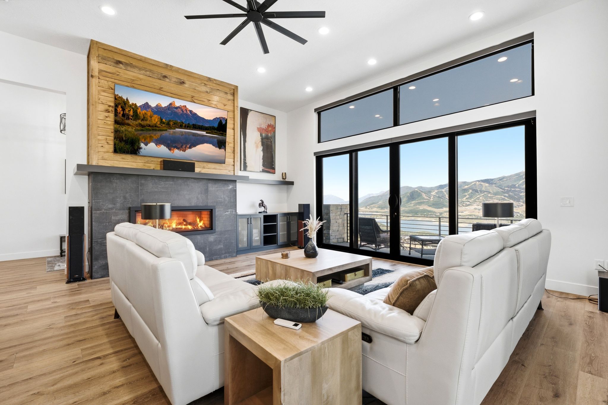 Spacious living area featuring expansive glass sliding doors, wood-finish flooring, a contemporary fireplace with stone surround, a wood-paneled accent wall, and recessed ceiling lighting