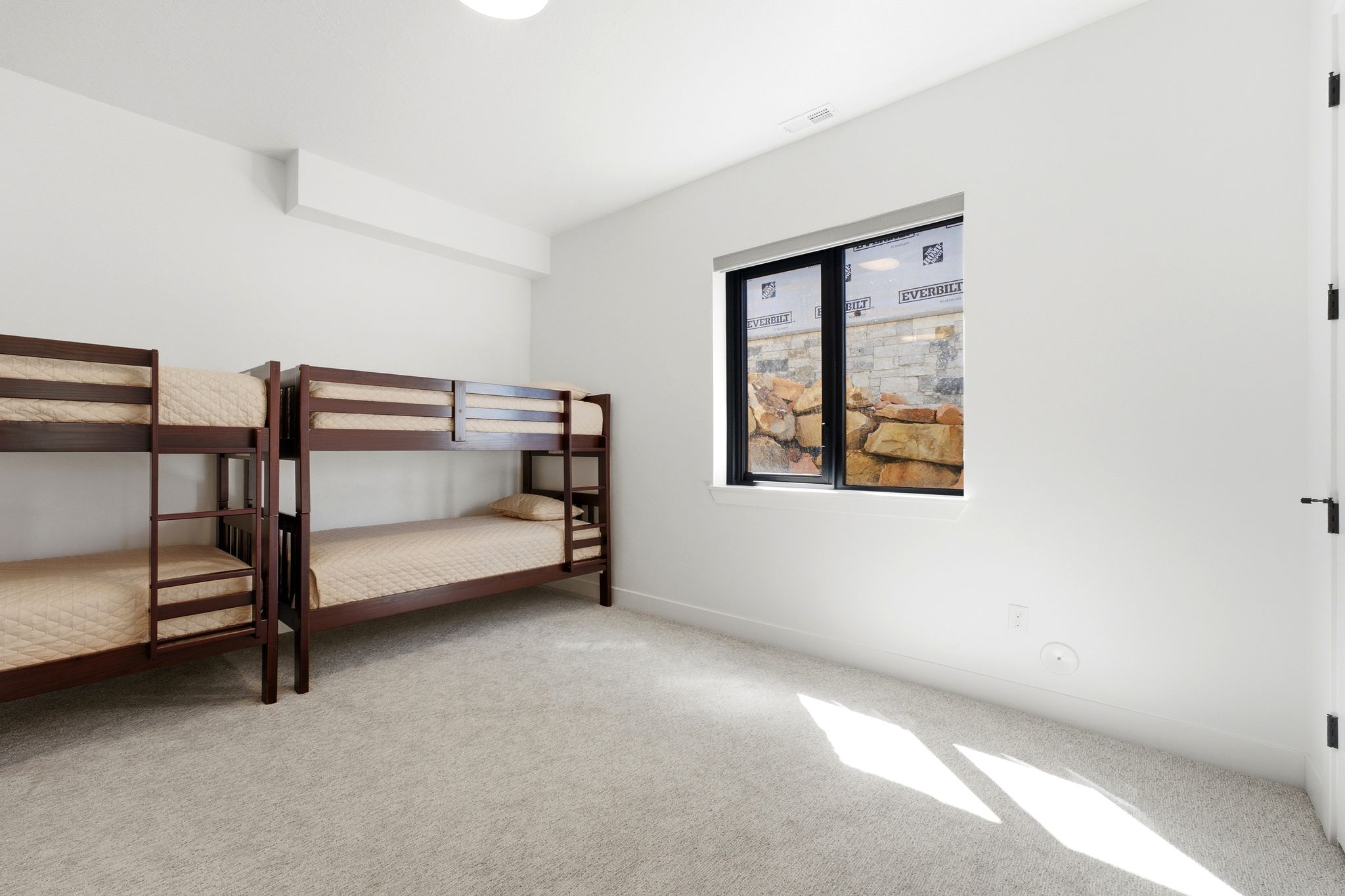 Bedroom featuring light gray carpet flooring, a single window with black trim, white painted walls, and a ceiling-mounted light fixture