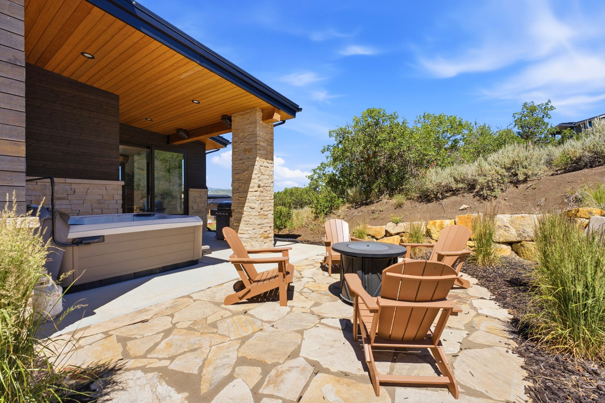 Expansive flagstone patio with a built-in hot tub, an outdoor fire pit, and a stone retaining wall