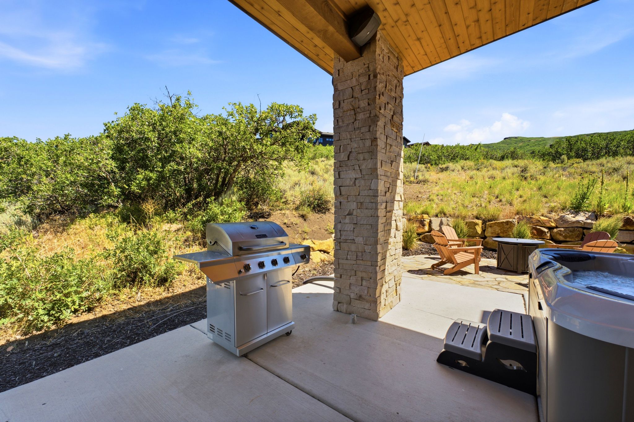 Covered patio featuring a wood-finished ceiling, stacked stone support pillar, and concrete flooring