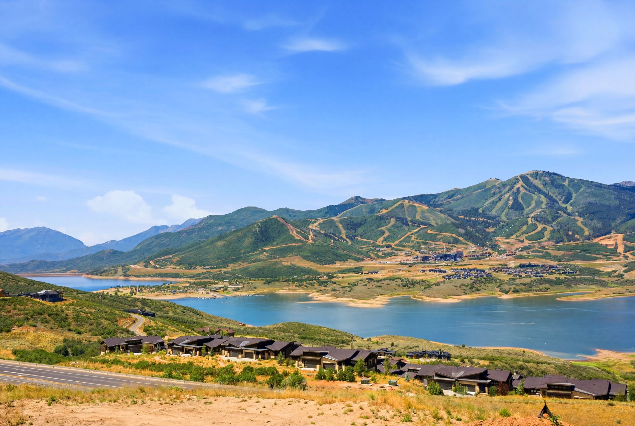 Expansive mountain and lake landscape featuring a clear blue sky, distant ski slopes, and a tranquil body of water
