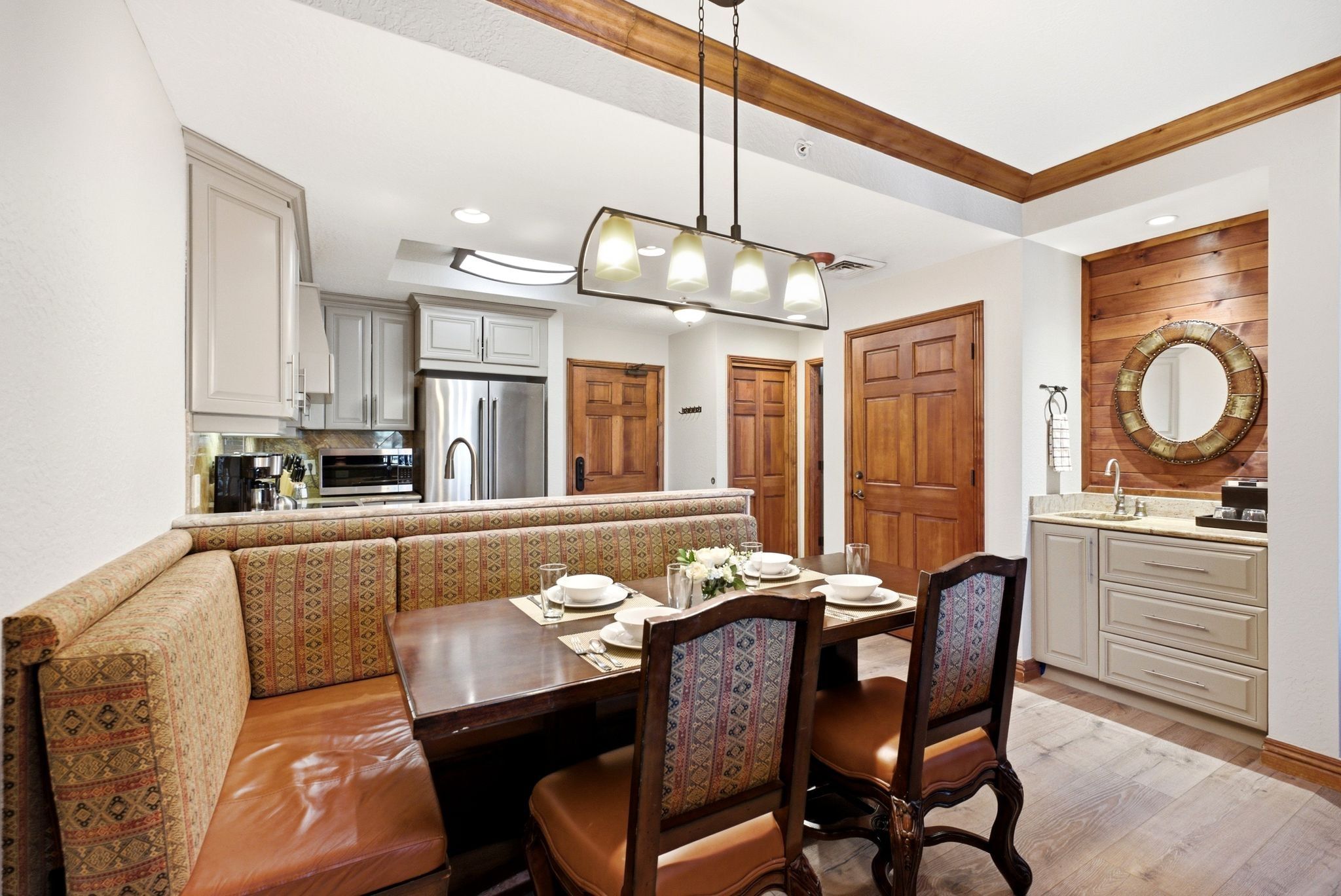 Open-concept dining area featuring a built-in banquette, wood-finish flooring, a contemporary chandelier, a wet bar with shaker-style cabinetry, and a kitchen with stainless steel appliances
