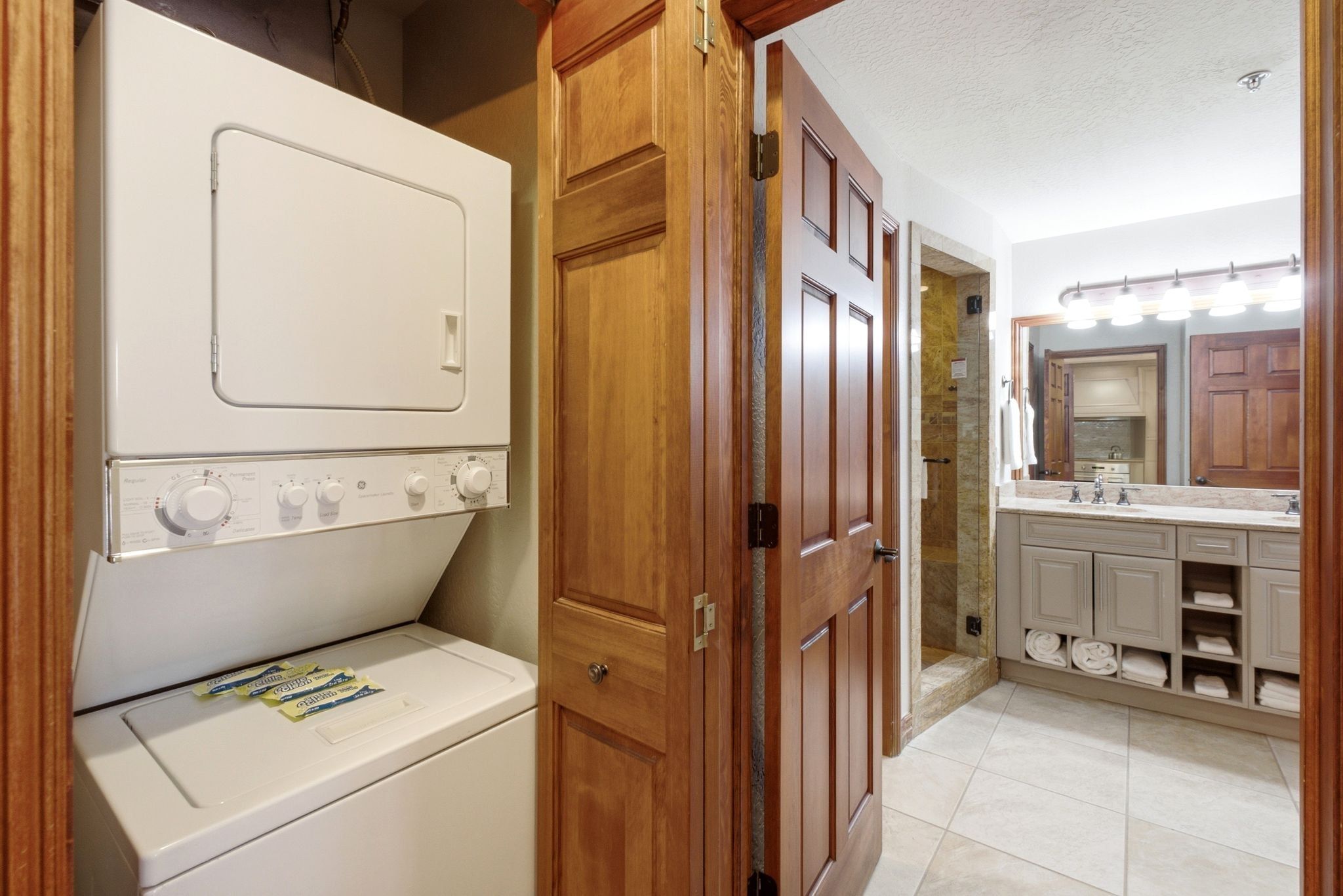 Stacked washer and dryer unit within a dedicated laundry closet featuring natural wood doors