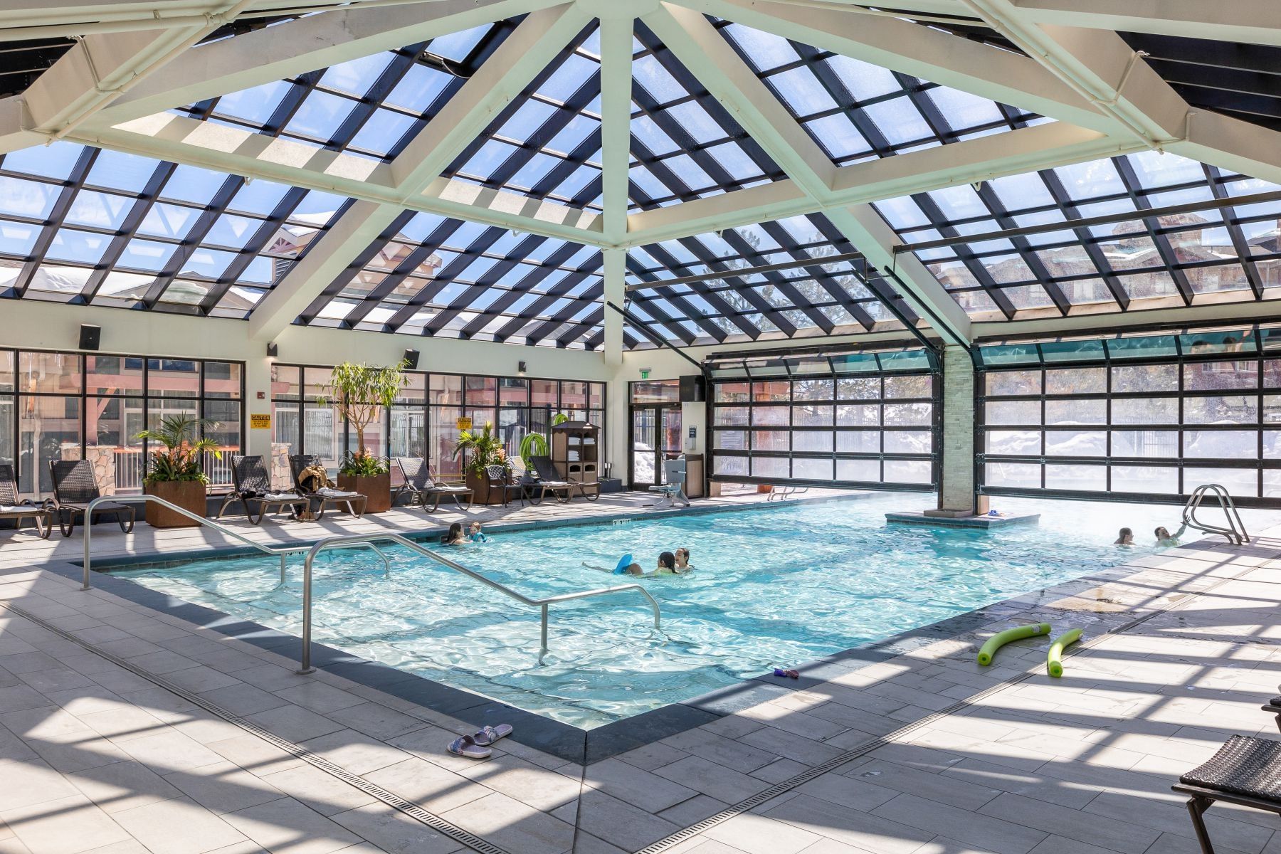 Indoor swimming pool featuring a glass-paneled ceiling, expansive window walls, and tiled flooring