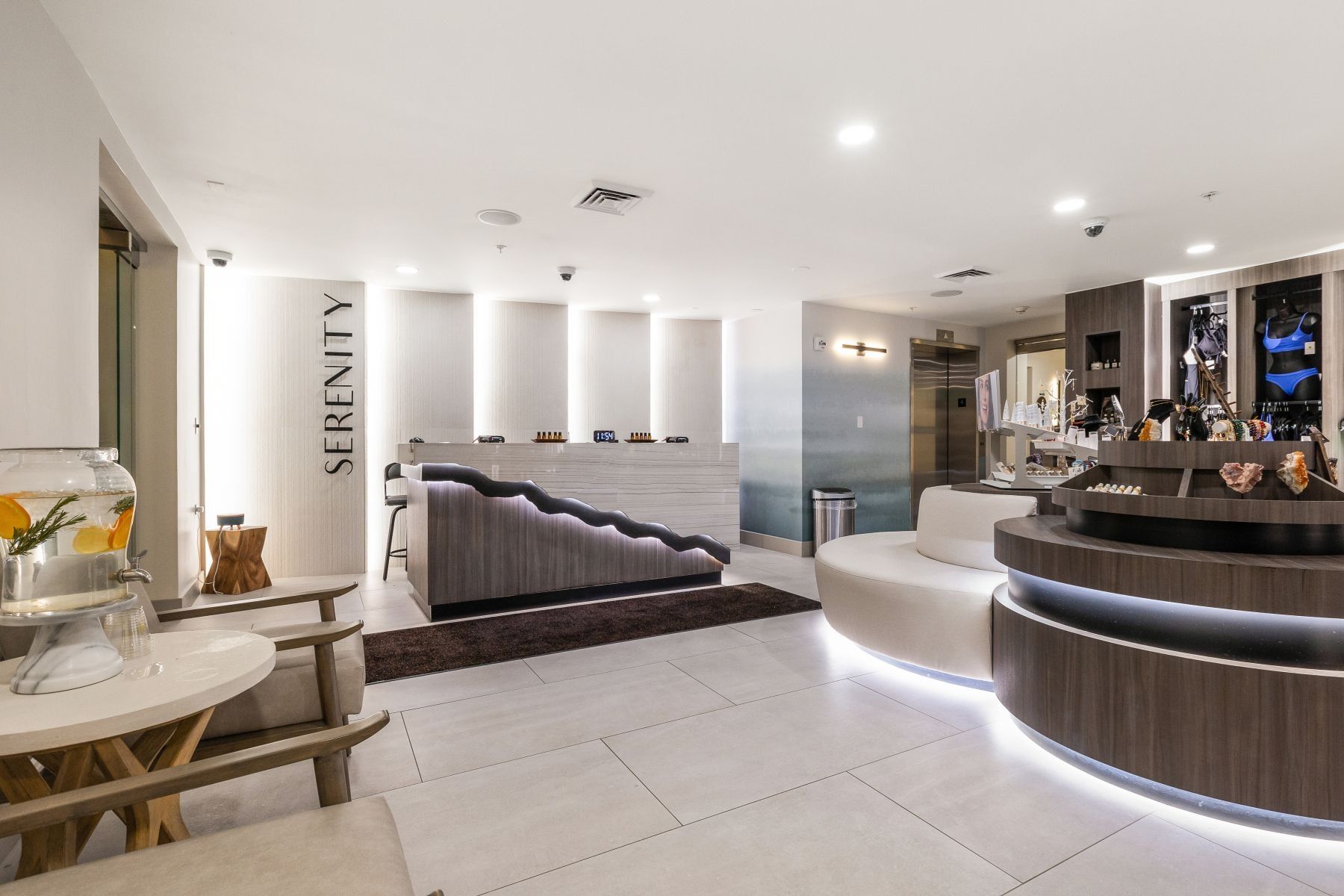 Modern reception area featuring light-toned large format floor tiles, integrated ceiling lighting, and a wood-finish reception desk with accent lighting