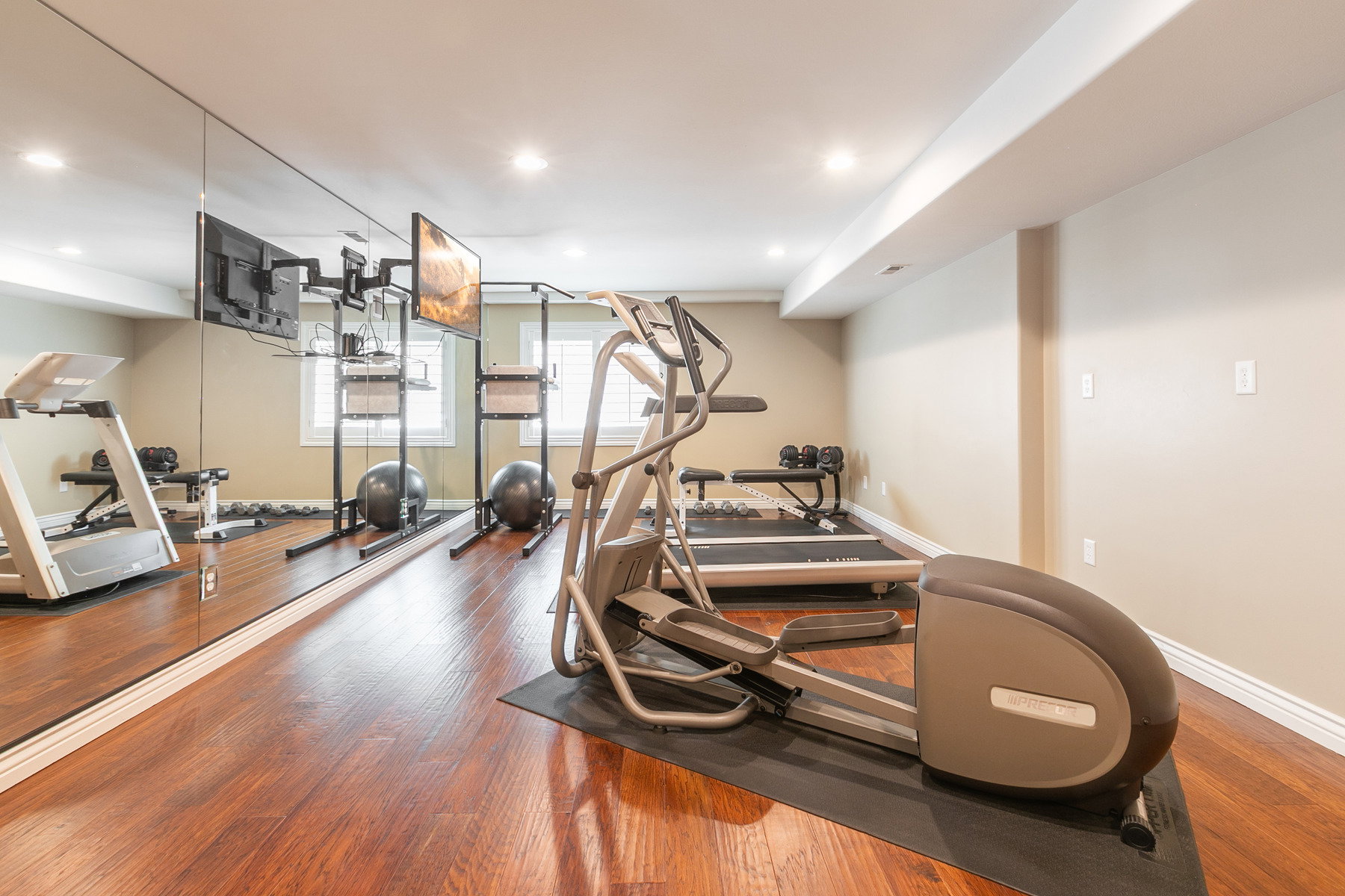 Dedicated fitness space featuring wood-finish flooring, recessed lighting, and a full-wall mirror