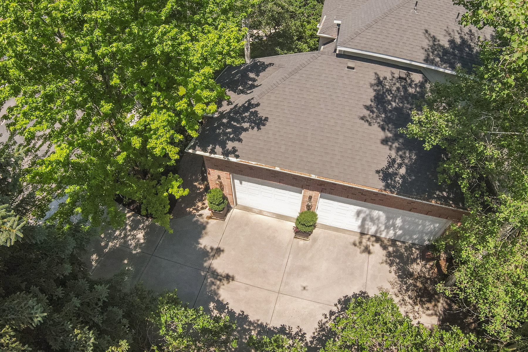 Three-car garage with brick facade, concrete driveway, and mature landscaping