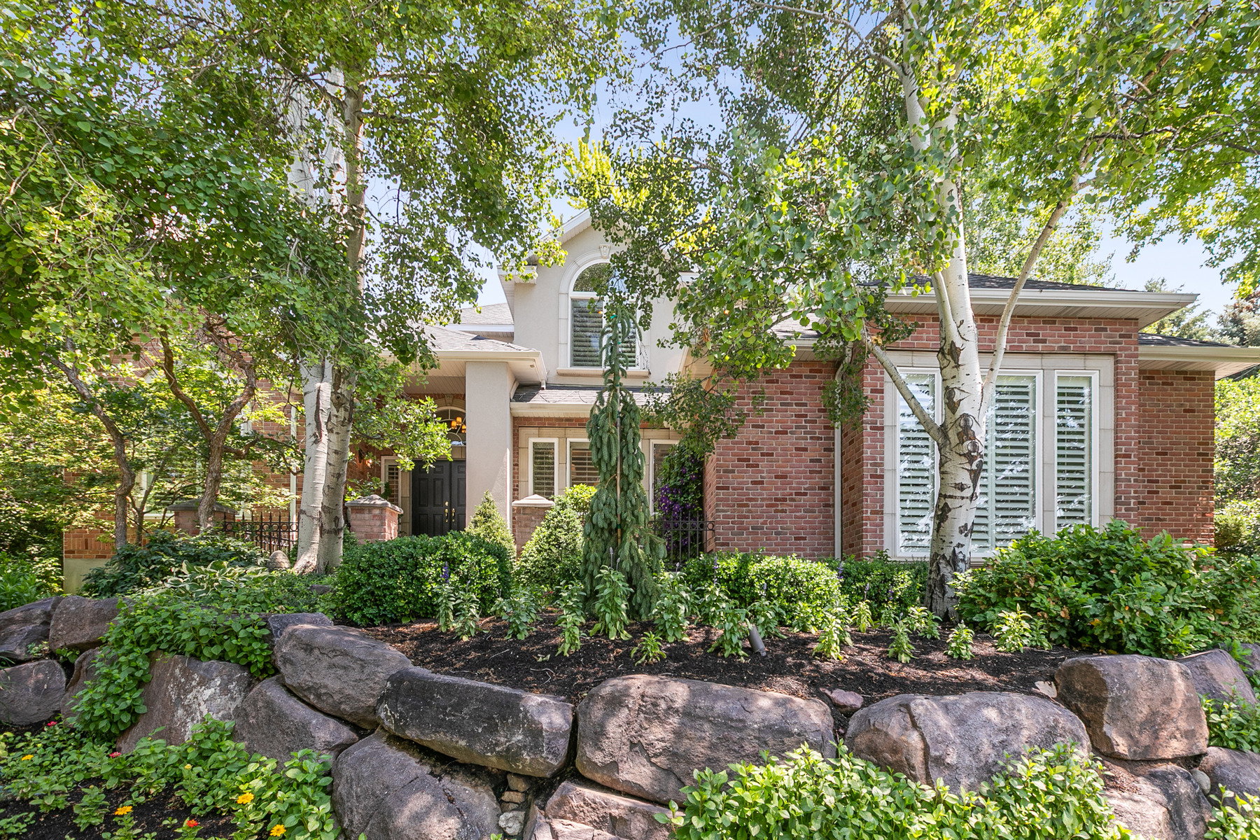 Brick and stucco exterior with multiple mature trees and an arched second-story window