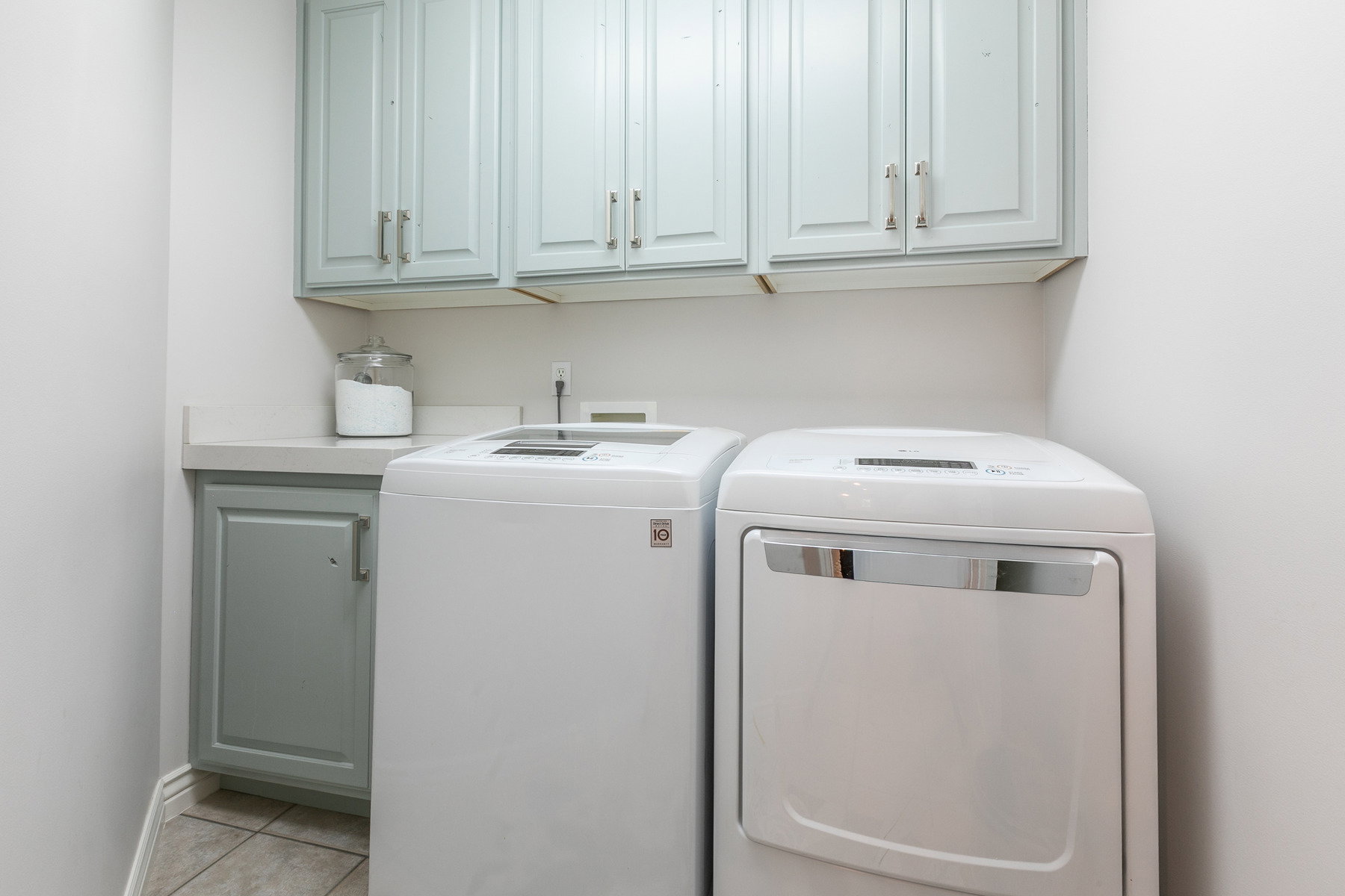 Laundry area featuring light blue cabinetry with brushed nickel hardware, a light-toned countertop, and tiled flooring