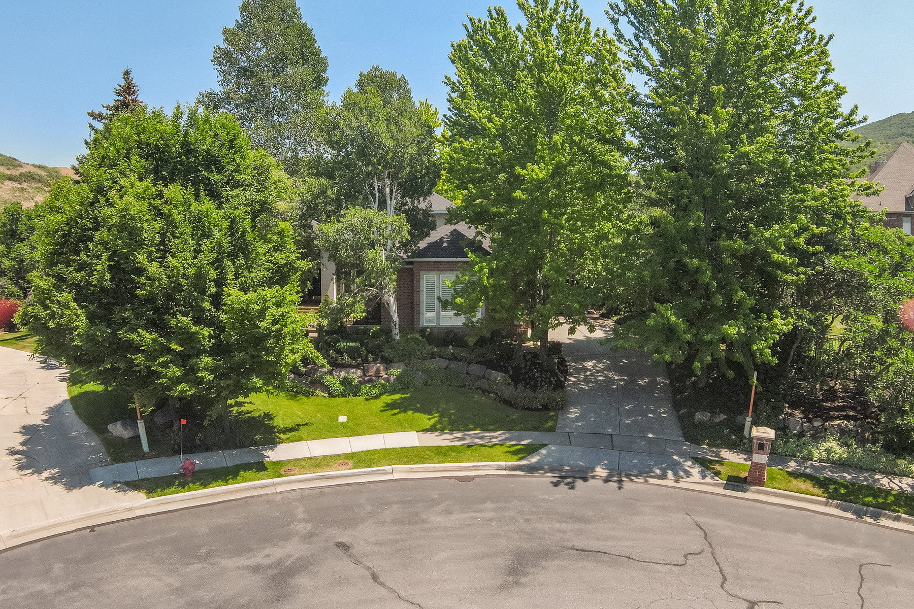 Brick exterior residence set back from the street, featuring mature trees providing extensive shade