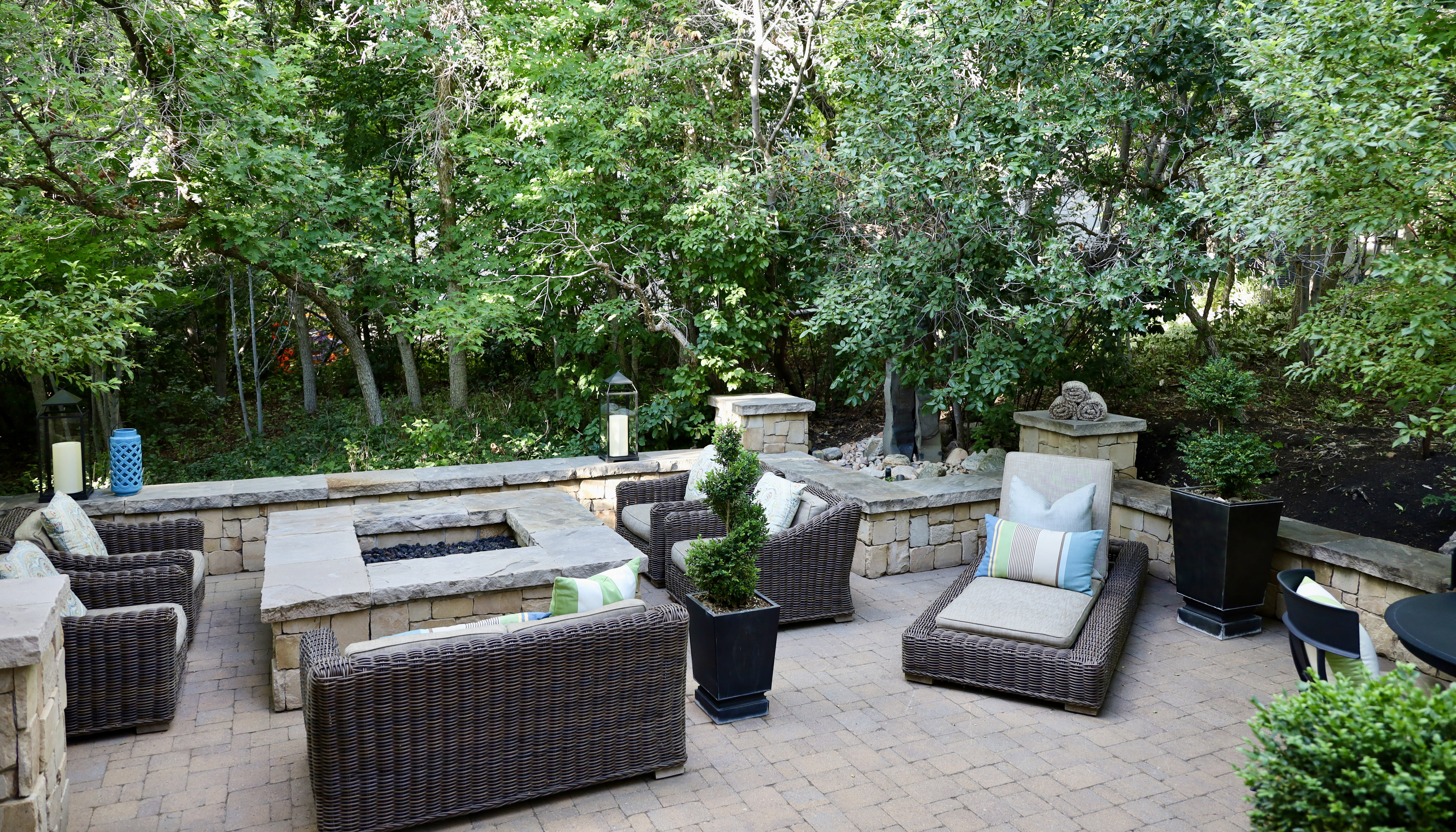 Paved patio with a built-in stone fire pit, stone retaining walls, and surrounding mature trees