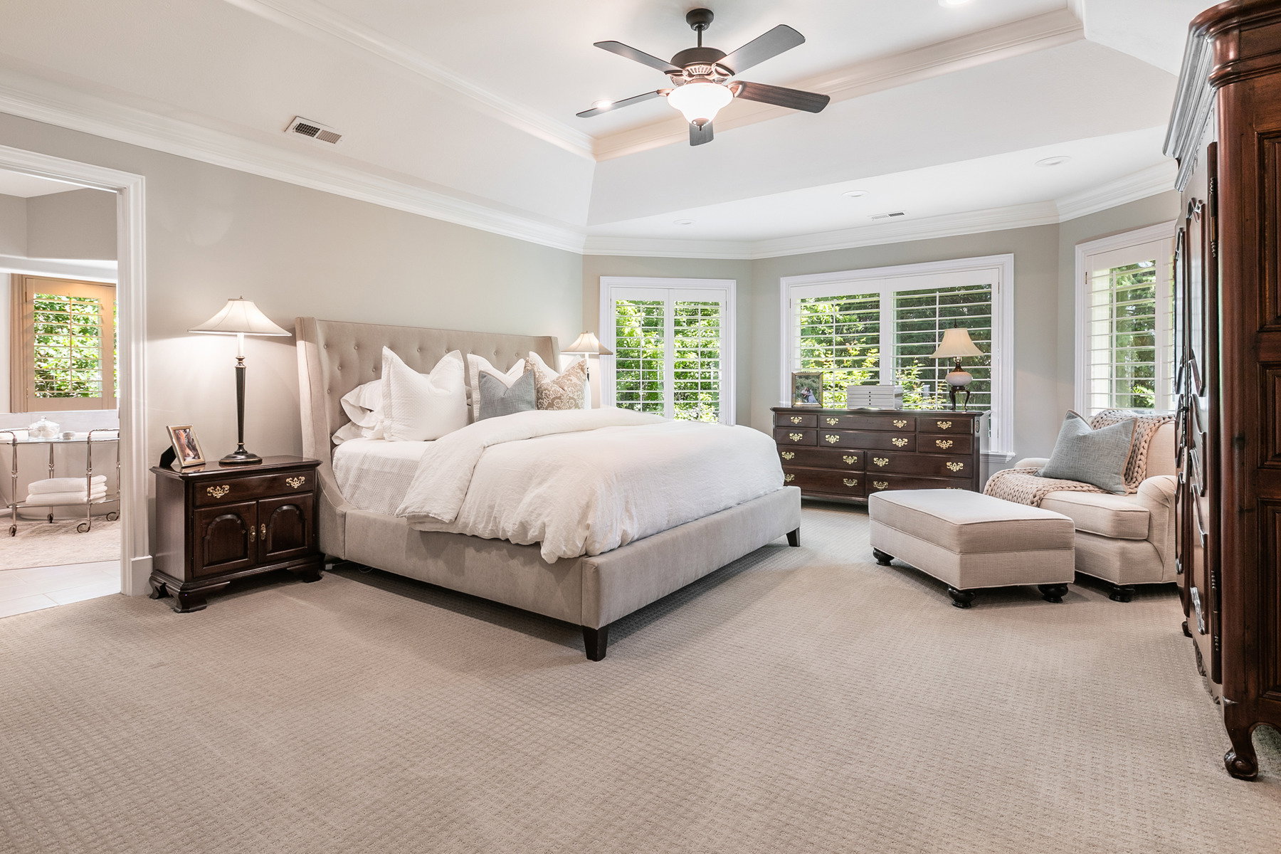 Spacious primary bedroom with tray ceiling, ceiling fan, and light-toned carpet flooring