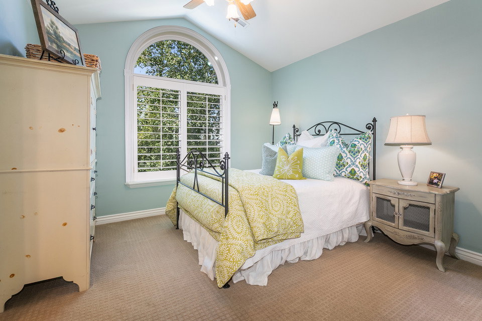 Bedroom featuring a large arched window with interior plantation shutters, vaulted ceiling, and carpeted flooring