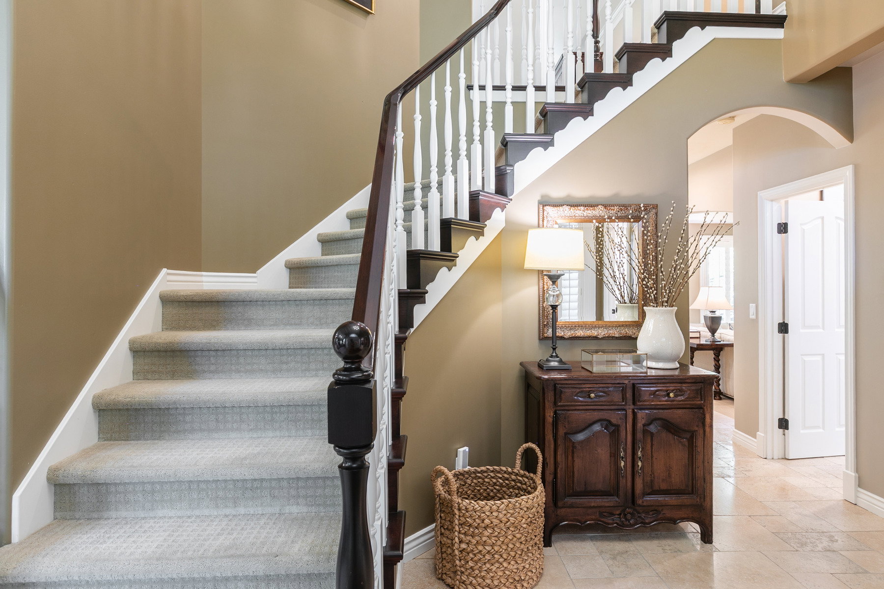 Carpeted staircase with white risers and dark wood handrail, featuring white balusters