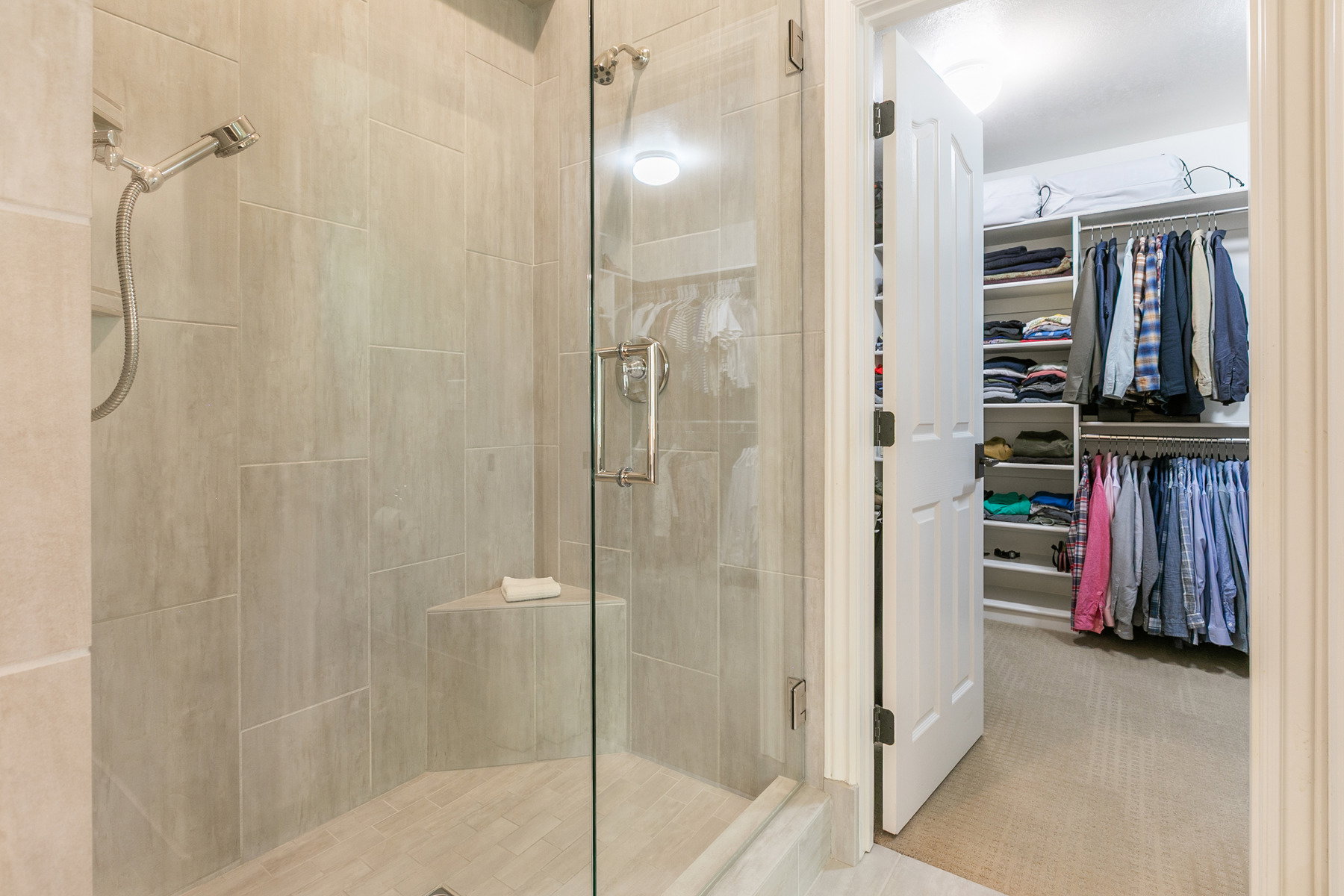 Walk-in shower with full-height tile surround, built-in corner bench, and frameless glass enclosure in the primary bathroom