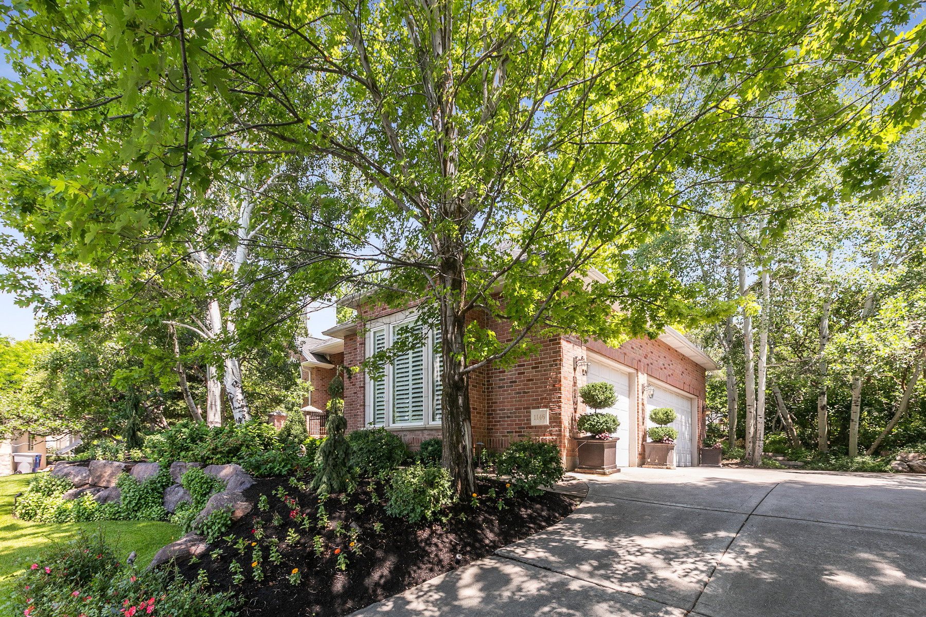 Brick exterior featuring white louvered shutters, an integrated three-car garage, and mature tree landscaping
