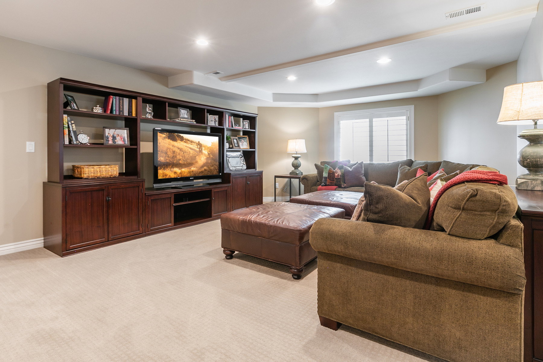 Built-in media console with storage cabinetry and open shelving, recessed lighting, carpeted flooring, and a tray ceiling detail