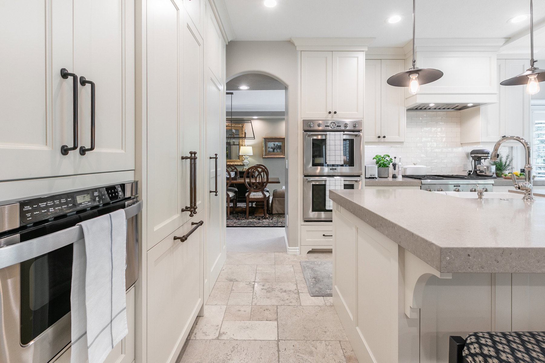 Gourmet kitchen featuring a large central island with a solid surface countertop, stainless steel double ovens, integrated refrigerator, white subway tile backsplash, and light-toned tile flooring