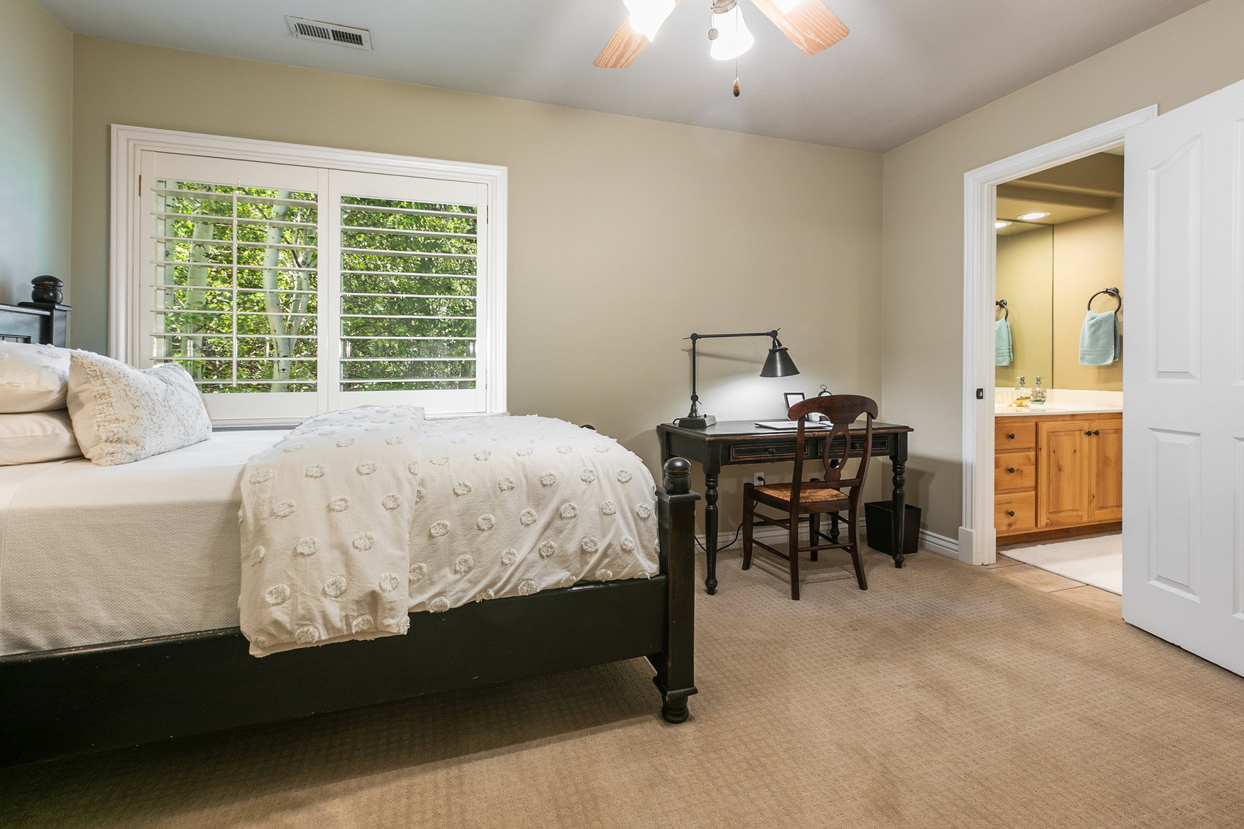 Bedroom featuring a window with white plantation shutters, neutral wall color, a ceiling fan with integrated lighting and an en suite