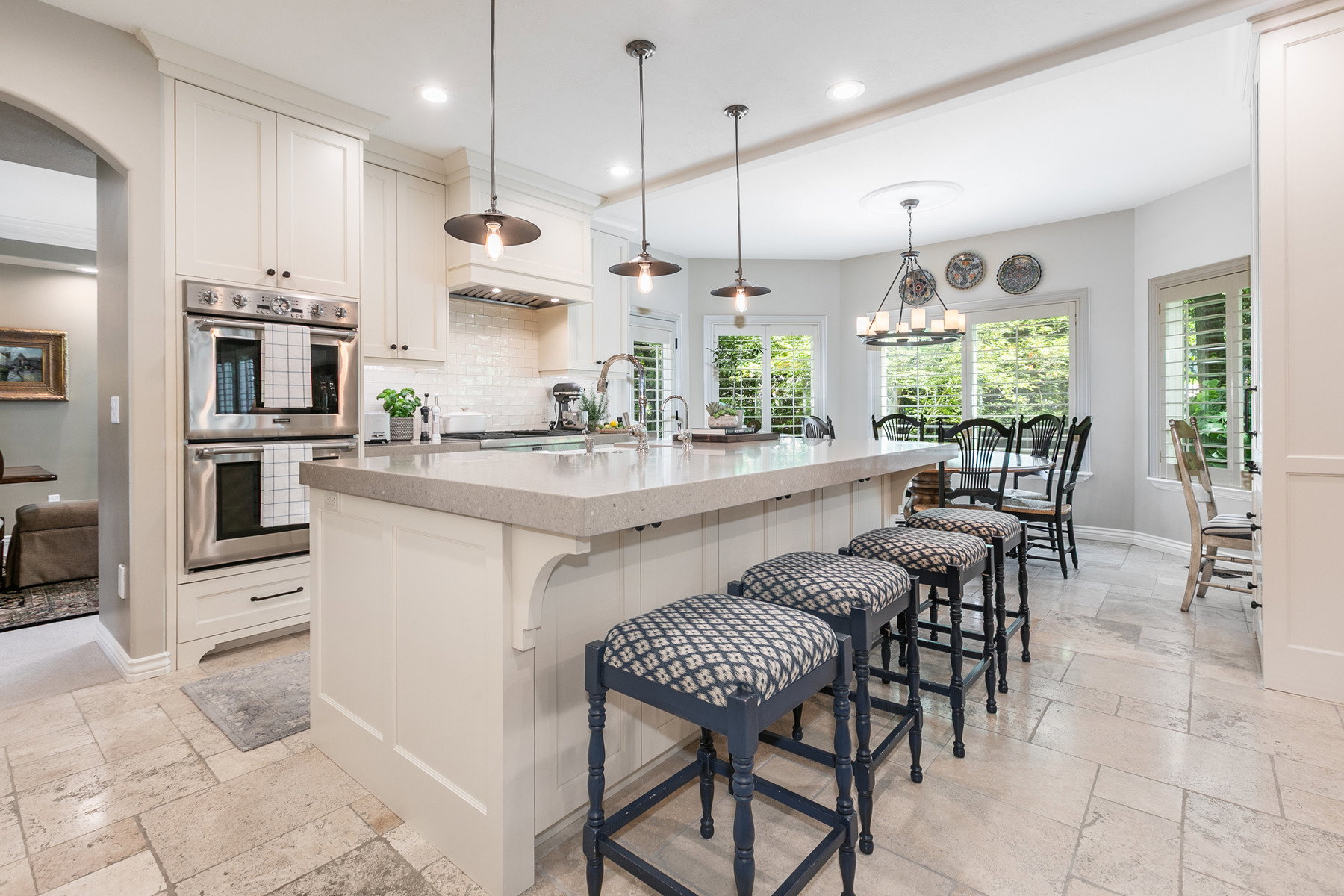 Gourmet kitchen featuring a substantial island with seating, double wall ovens, a tiled backsplash, built-in cabinetry, and pendant lighting