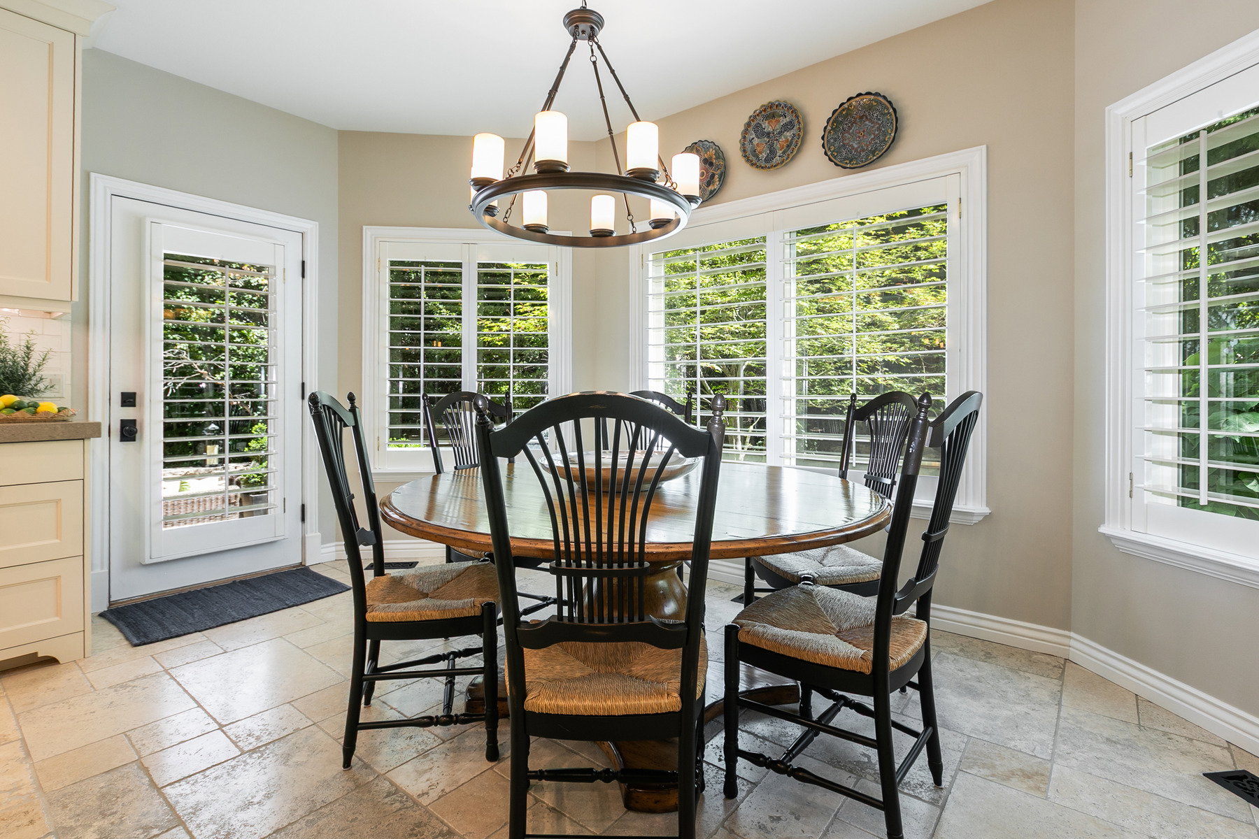 Bright dining area featuring a bay window with plantation shutters, a glass-paned door, and large format tile flooring