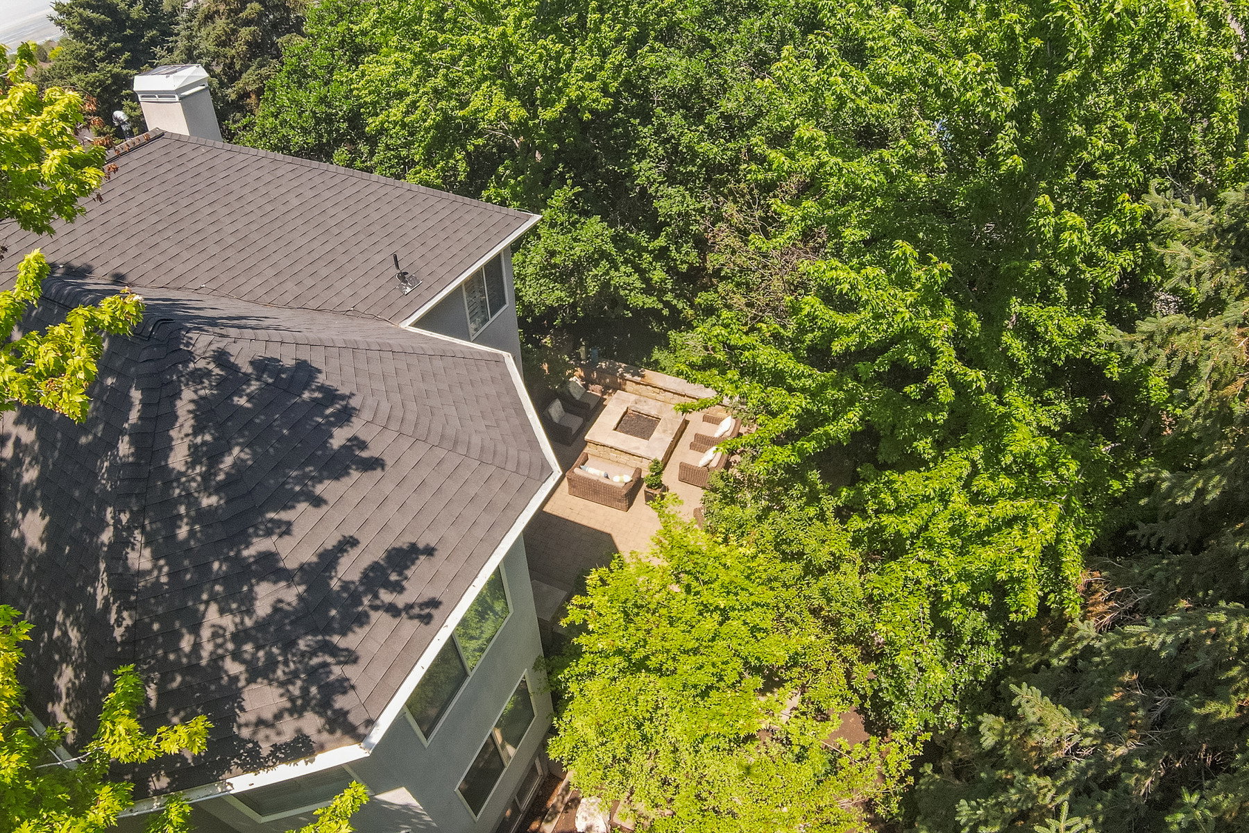 Exterior featuring a dark shingle roof, chimney, and multiple windows. Ariel of mature trees in backyard and private patio.