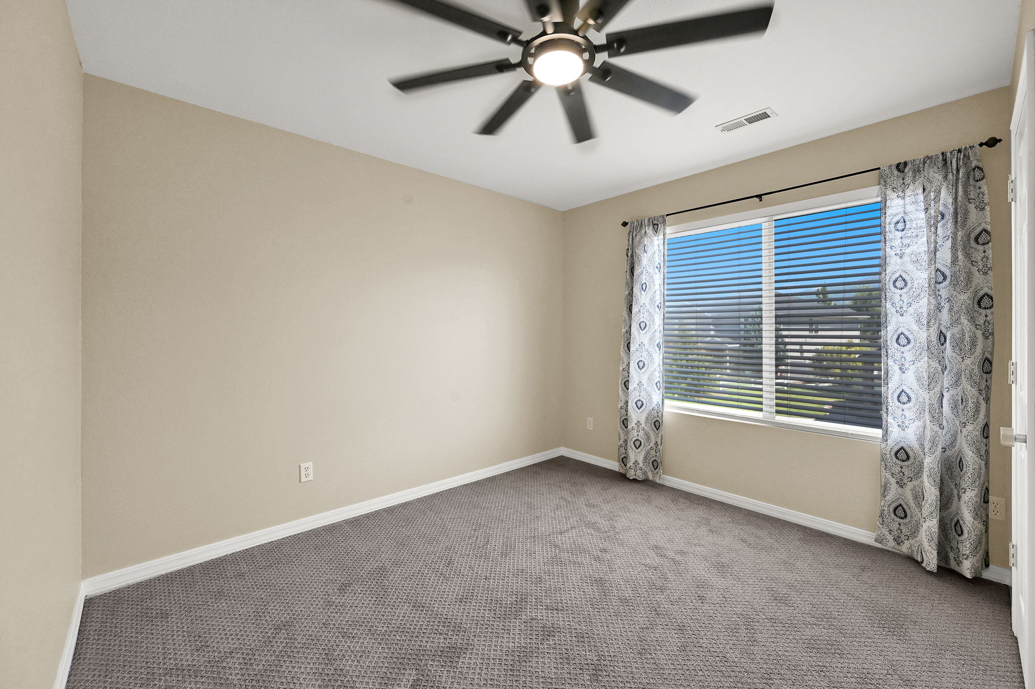 BEDROOM 3 Spacious room featuring neutral-toned walls, grey carpeting, a multi-pane window with horizontal blinds, and a ceiling fan with integrated lighting