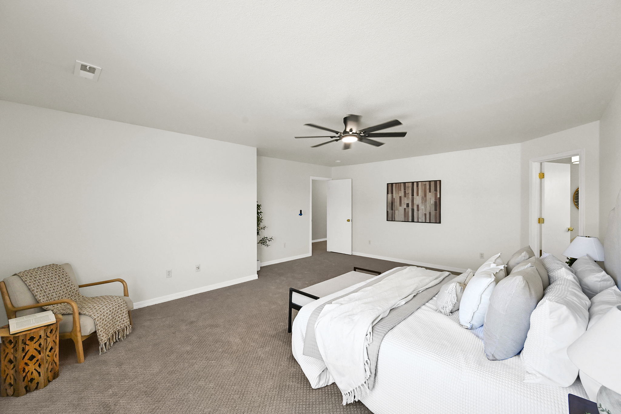 Spacious primary bedroom featuring modern patterned warm sand colored carpeting, white walls, a ceiling fan with integrated lighting, and two white doors with gold-toned hardware