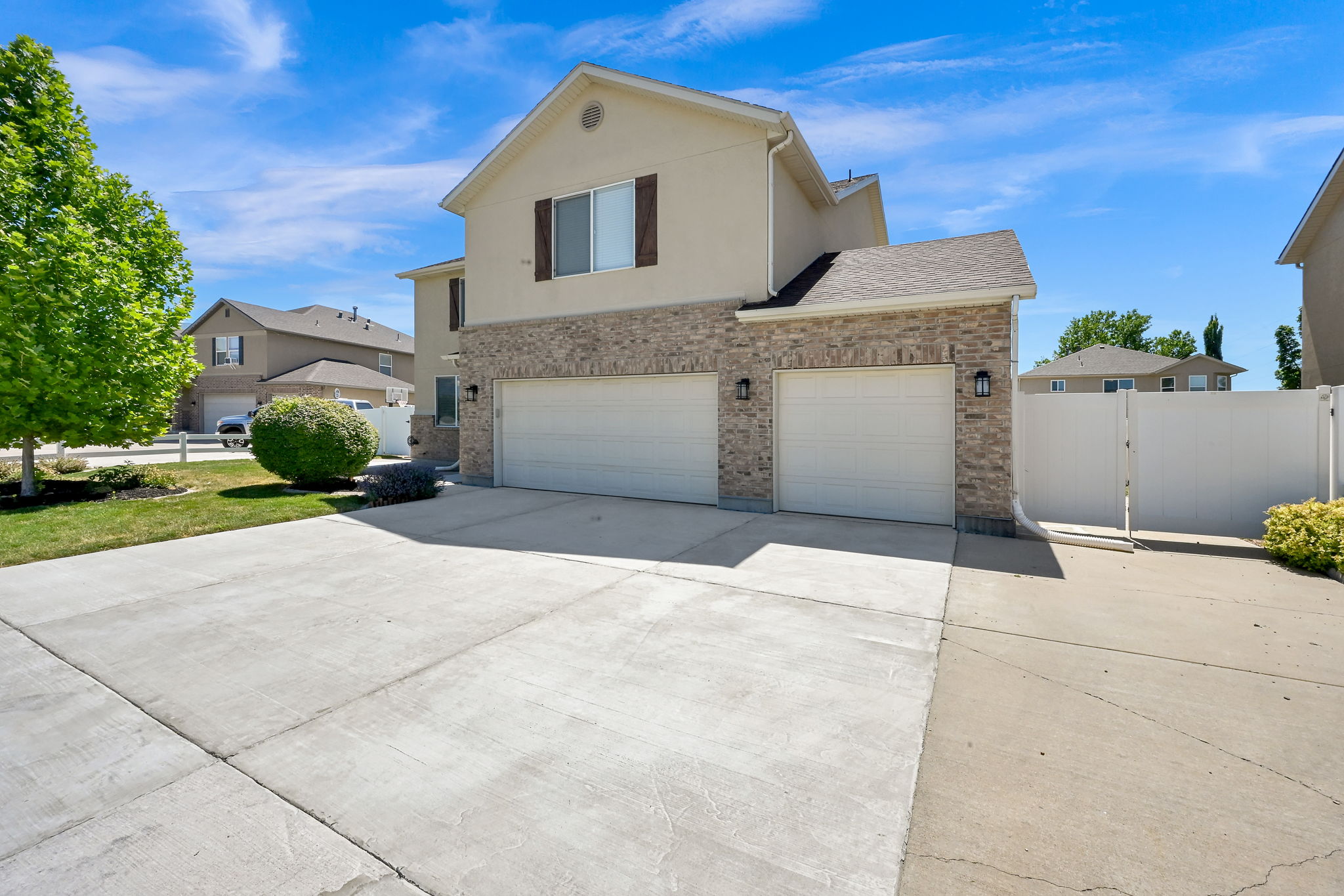 Two-story residence featuring a mixed-material exterior of stucco and brick-veneer, an attached two-car garage with white doors, a concrete driveway, and a partially visible white privacy fence
