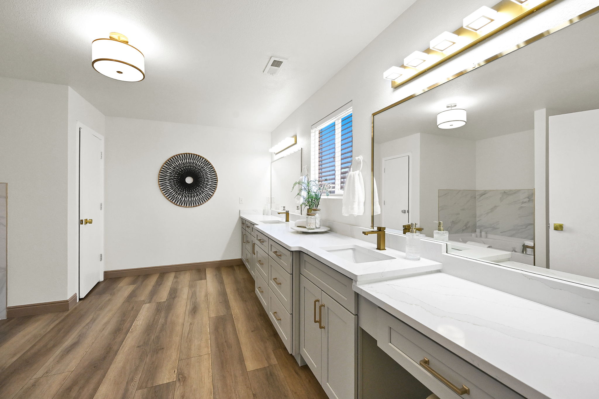 Expansive vanity featuring dual undermount sinks with brushed gold fixtures, white countertops, and extensive gray cabinetry