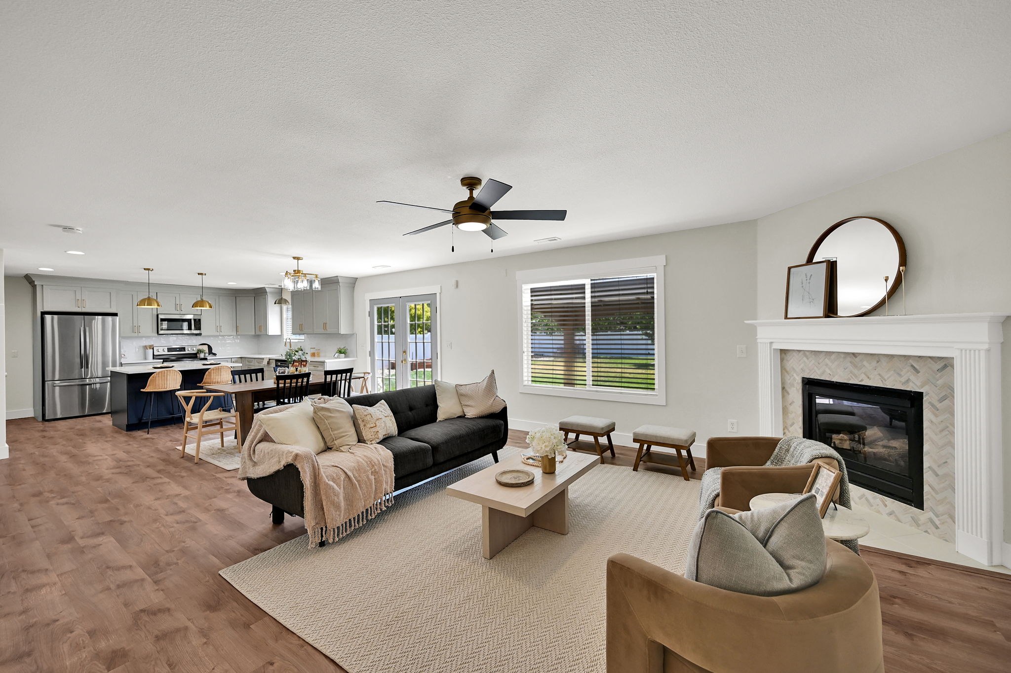 Spacious open-concept living area featuring wood-finish flooring, a contemporary fireplace with a herringbone tile surround, and a gold and black ceiling fan