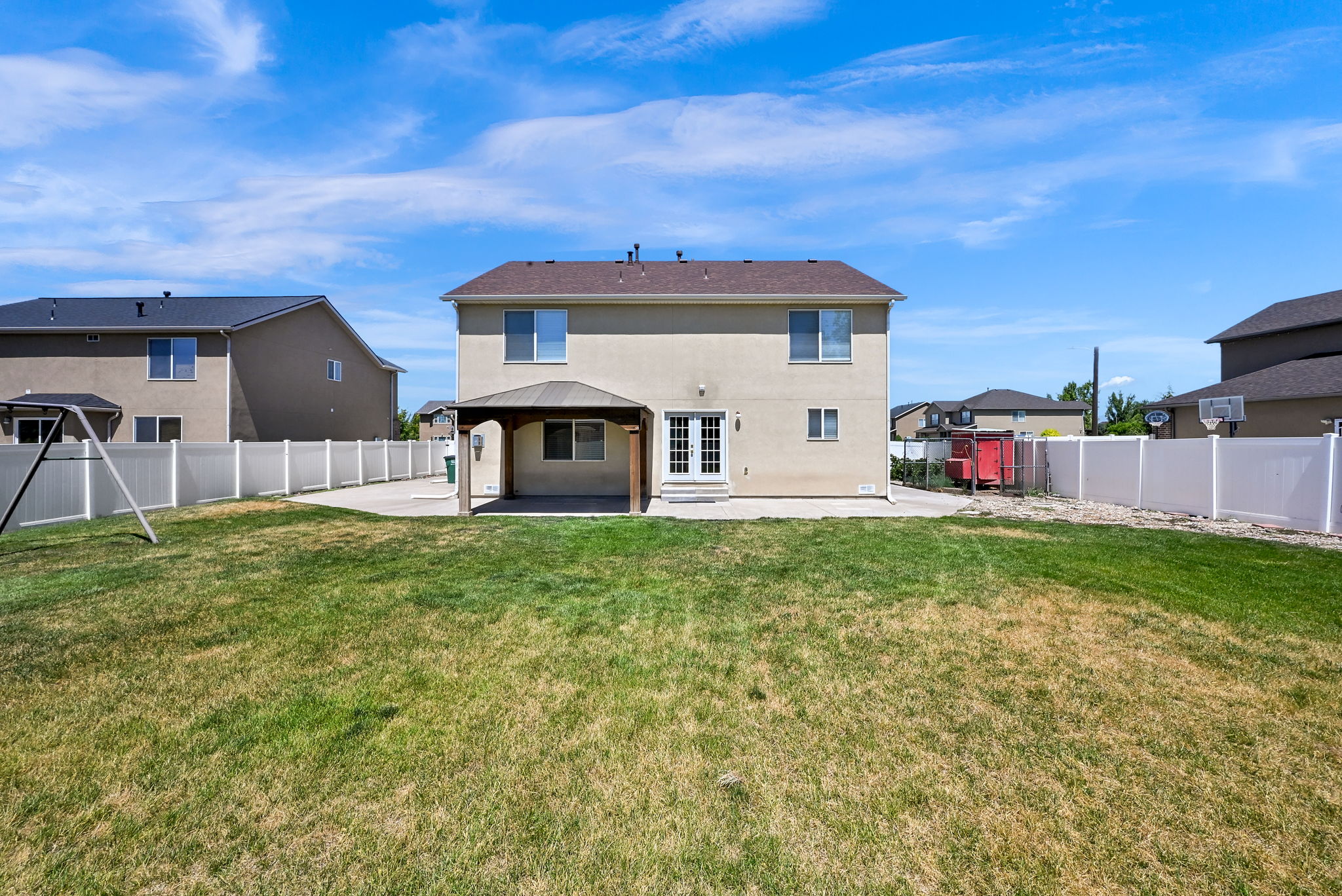 Large fully fenced yard. Rear exterior featuring a covered patio, double French doors, a manicured lawn, and white privacy fencing