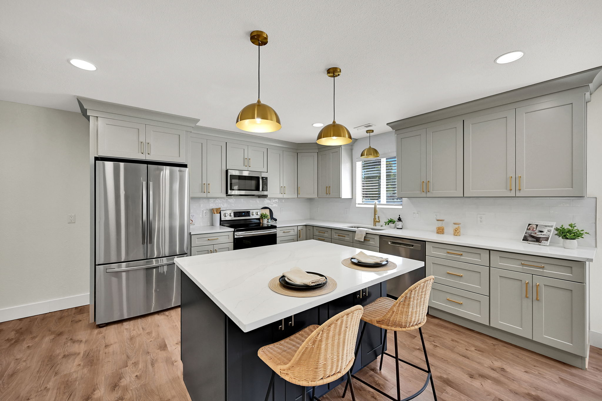 Kitchen featuring a central island with a white countertop and navy base, recessed lighting, brass pendant lights, stainless steel appliances, and wood-finish flooring