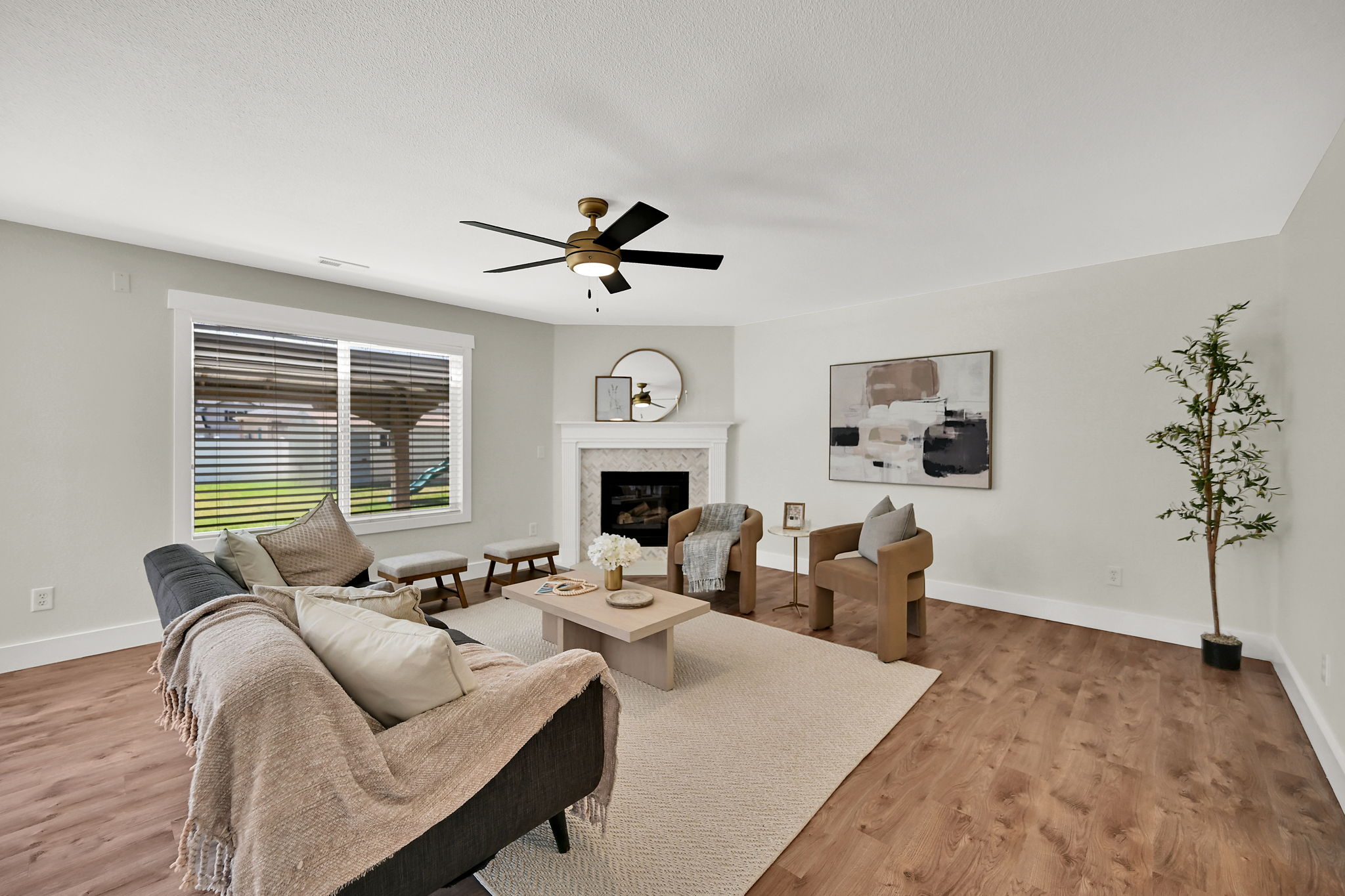 Spacious living area featuring wood-finish flooring, a corner fireplace with a white mantel, and a ceiling fan with integrated lighting