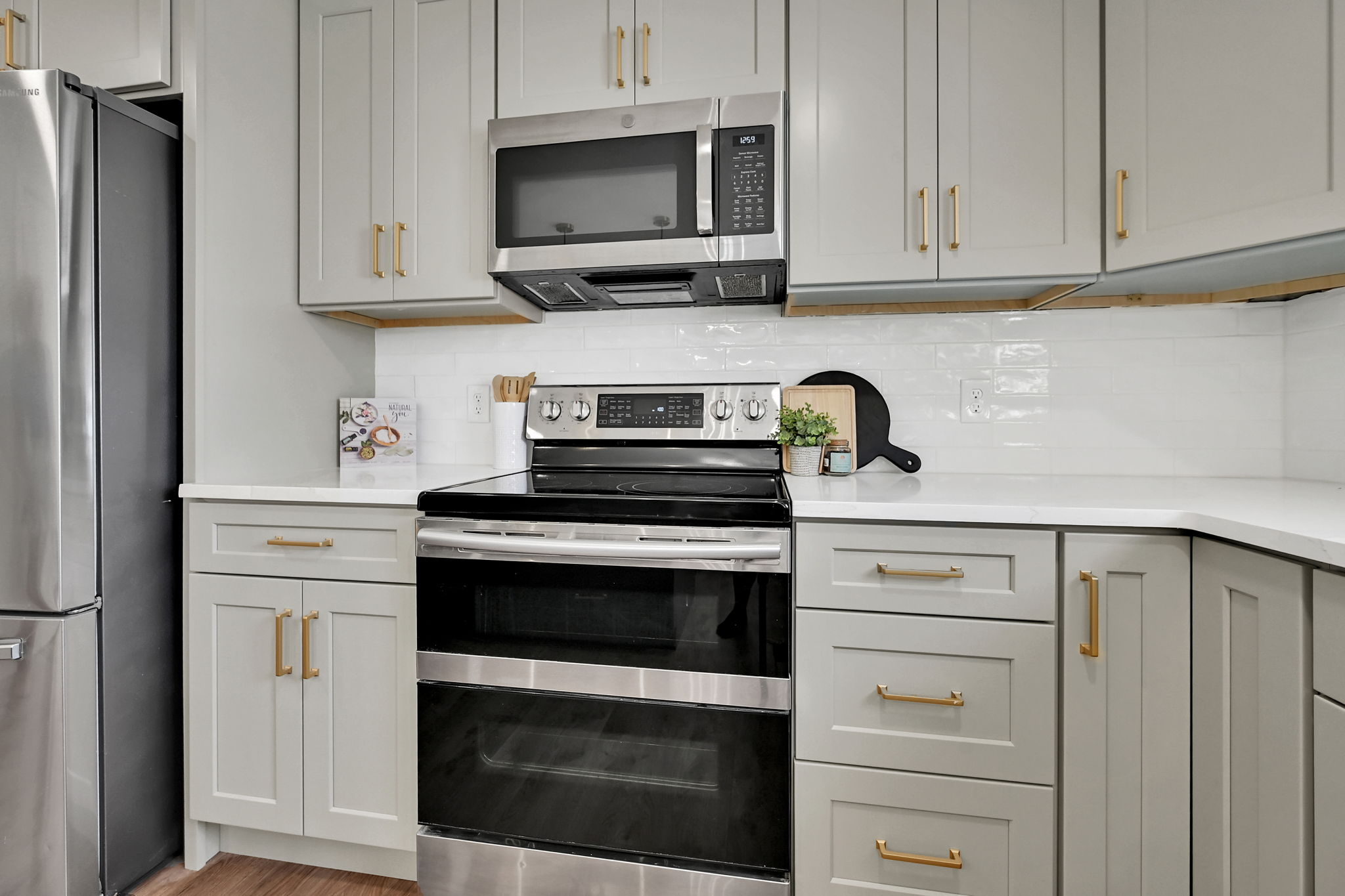 Dual Range with 2 baking compartments. Kitchen featuring light gray cabinetry with gold-tone hardware, white countertops, a white subway tile backsplash, stainless steel appliances, and wood-finish flooring