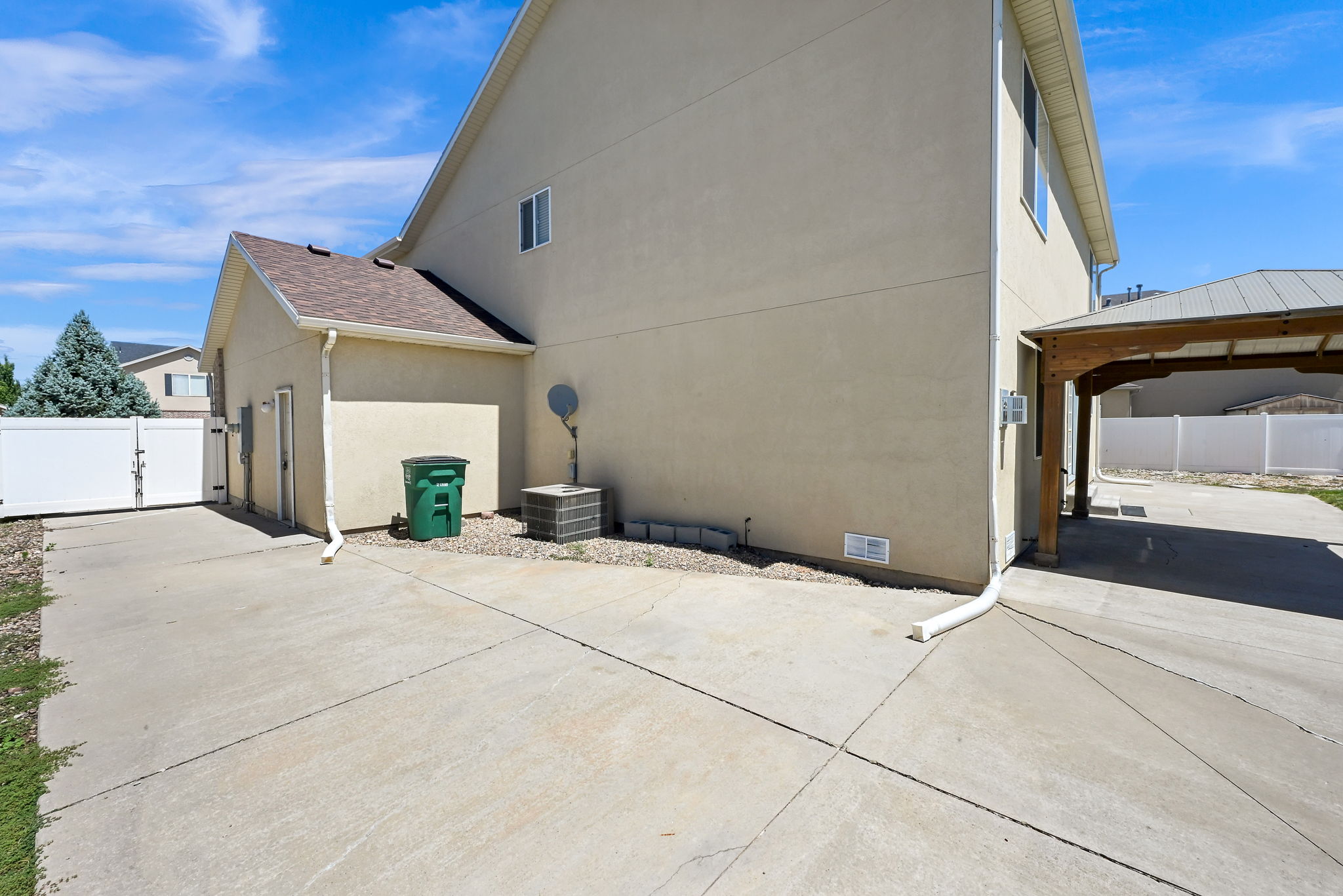 Expansive concrete driveway and side yard featuring a white vinyl fence and gate