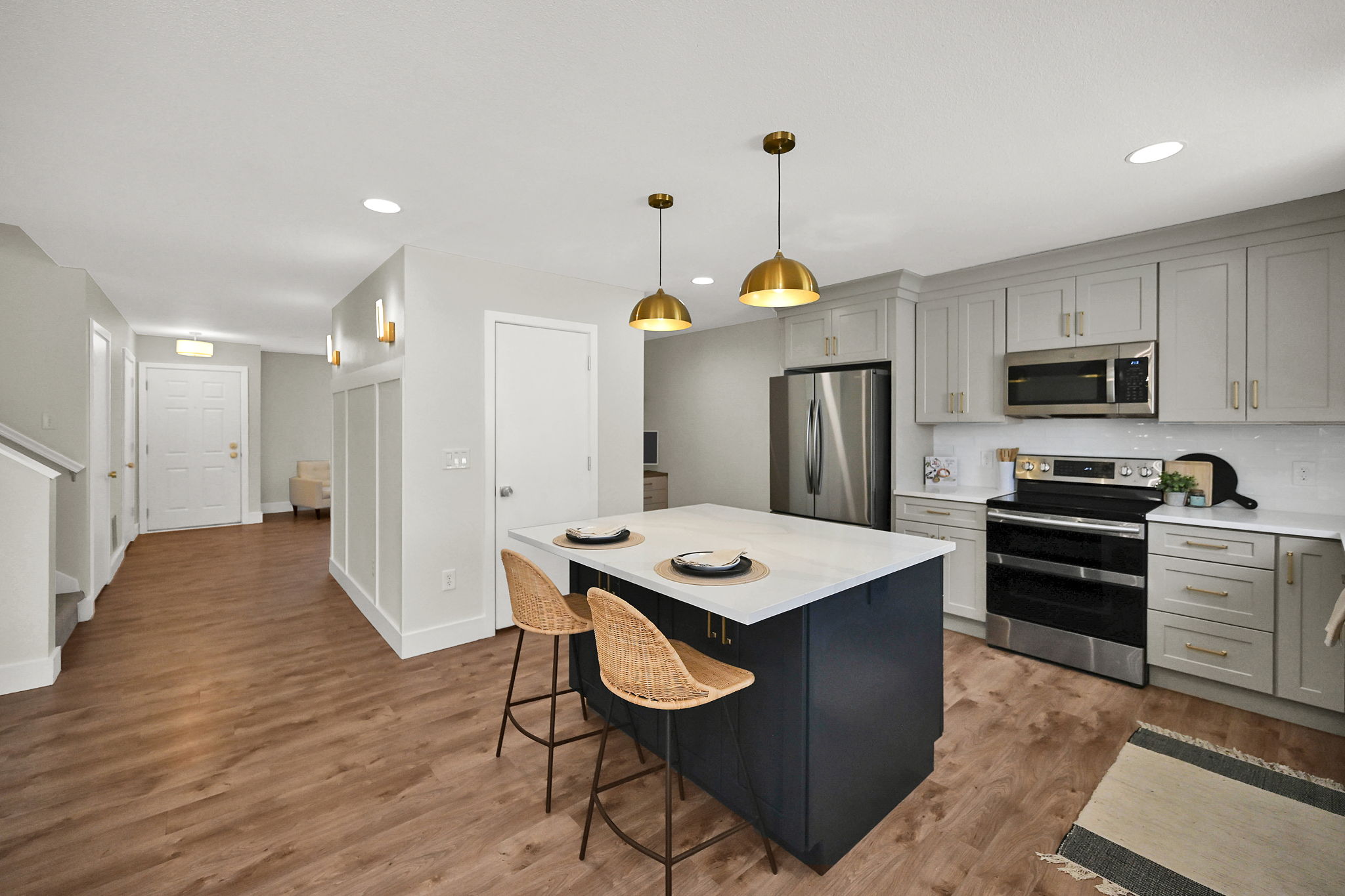 Kitchen featuring a navy island with a white countertop, gold-toned pendant lighting, wood-finish flooring, light grey cabinetry, and stainless steel appliances