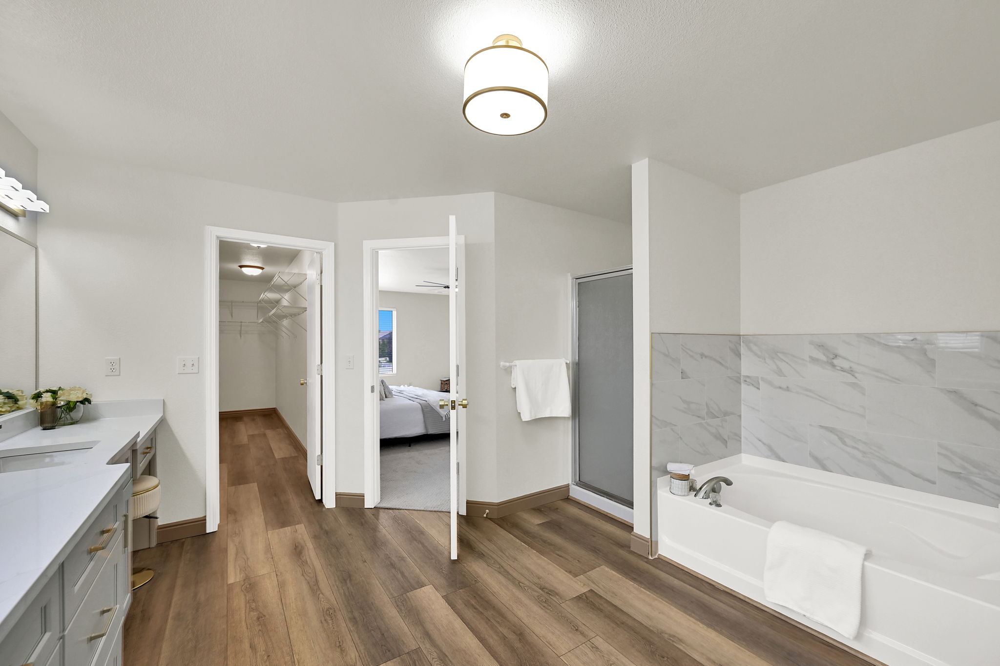 Bathroom featuring wood-finish flooring, a double vanity with quartz countertops, an oversized soaking tub with marble tile surround surround, and a glass-enclosed shower