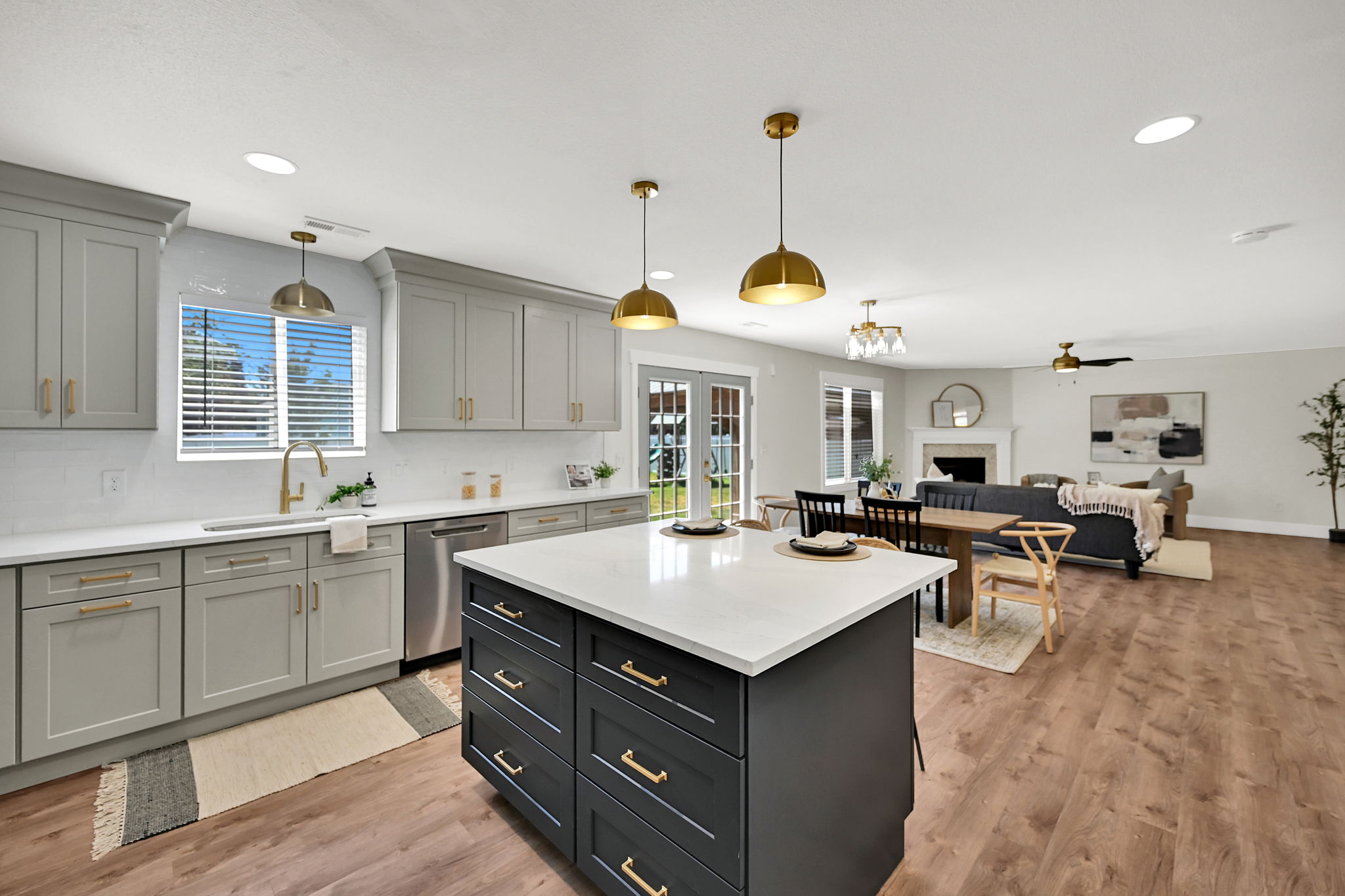 Open-concept living space featuring a gourmet kitchen with a central island, light gray cabinetry, white countertops, and wood-finish flooring throughout