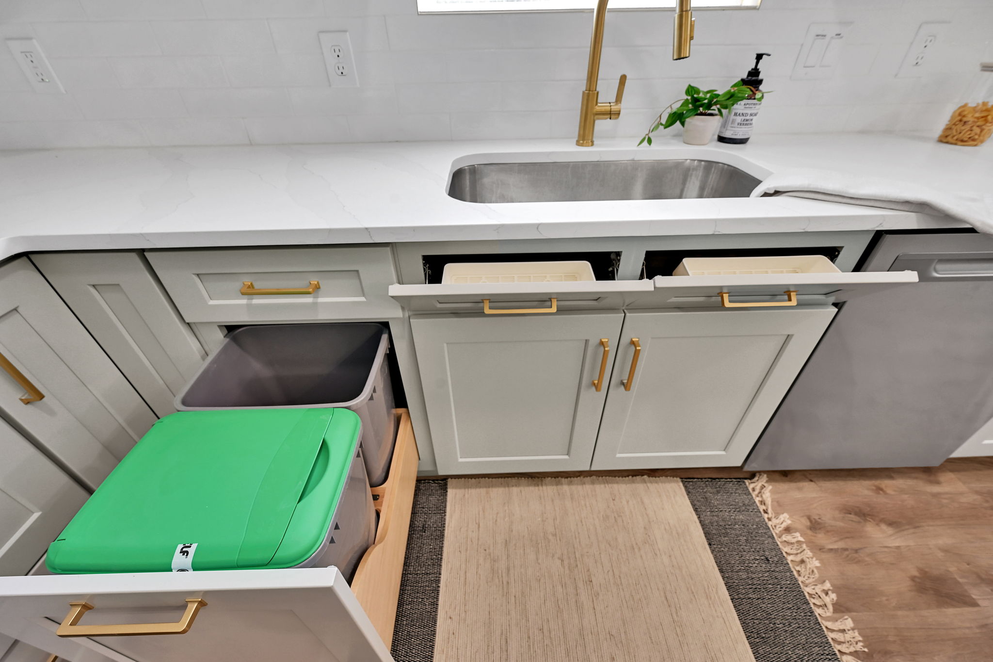 Light gray shaker-style cabinetry with gold-tone hardware, featuring a pull-out waste and recycle bin drawer
