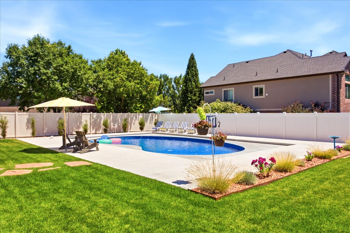 Expansive backyard featuring a curved swimming pool with concrete decking, surrounded by a white privacy fence