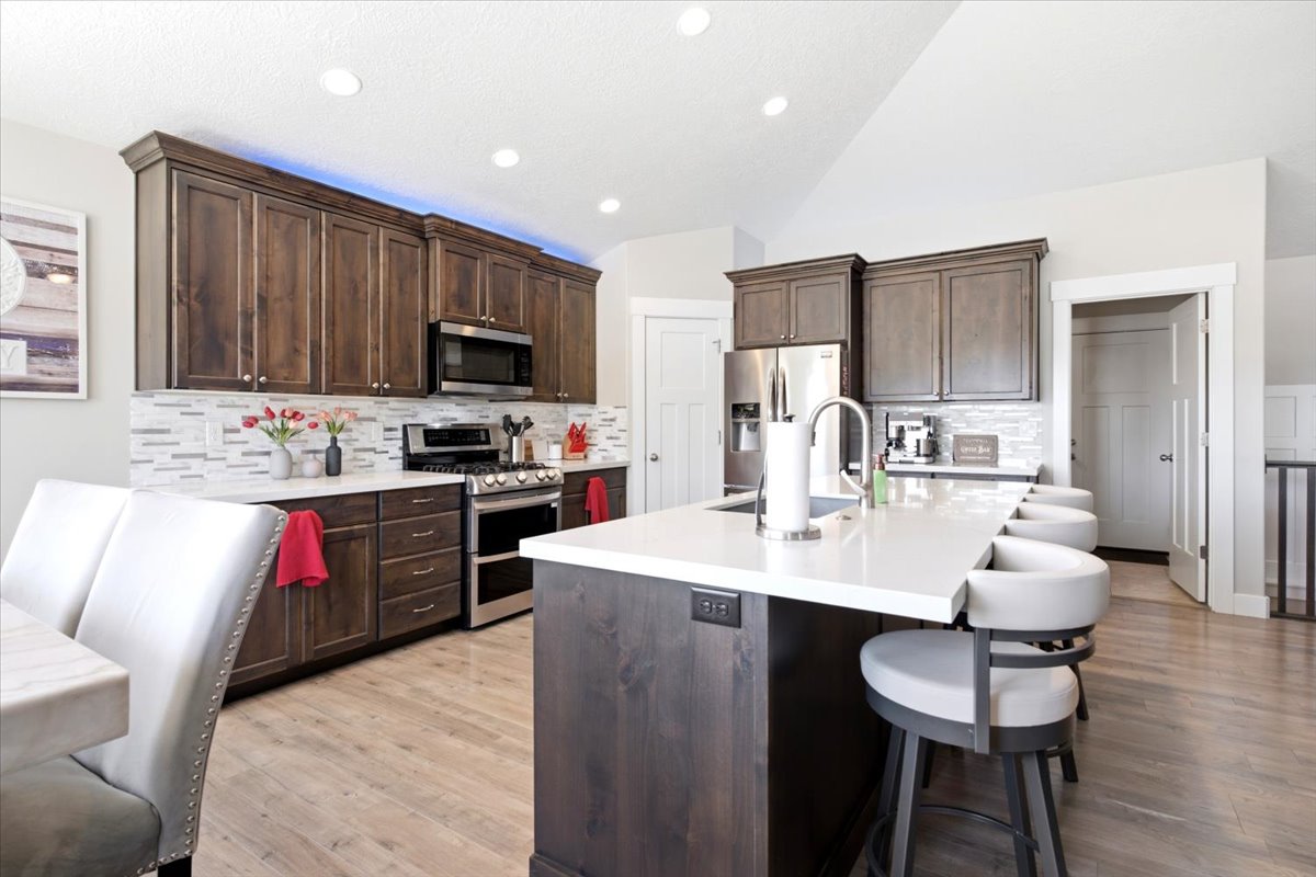 Spacious kitchen featuring dark wood-finish cabinetry, stainless steel appliances, a white tile backsplash, a large kitchen island with seating, and light wood-finish flooring