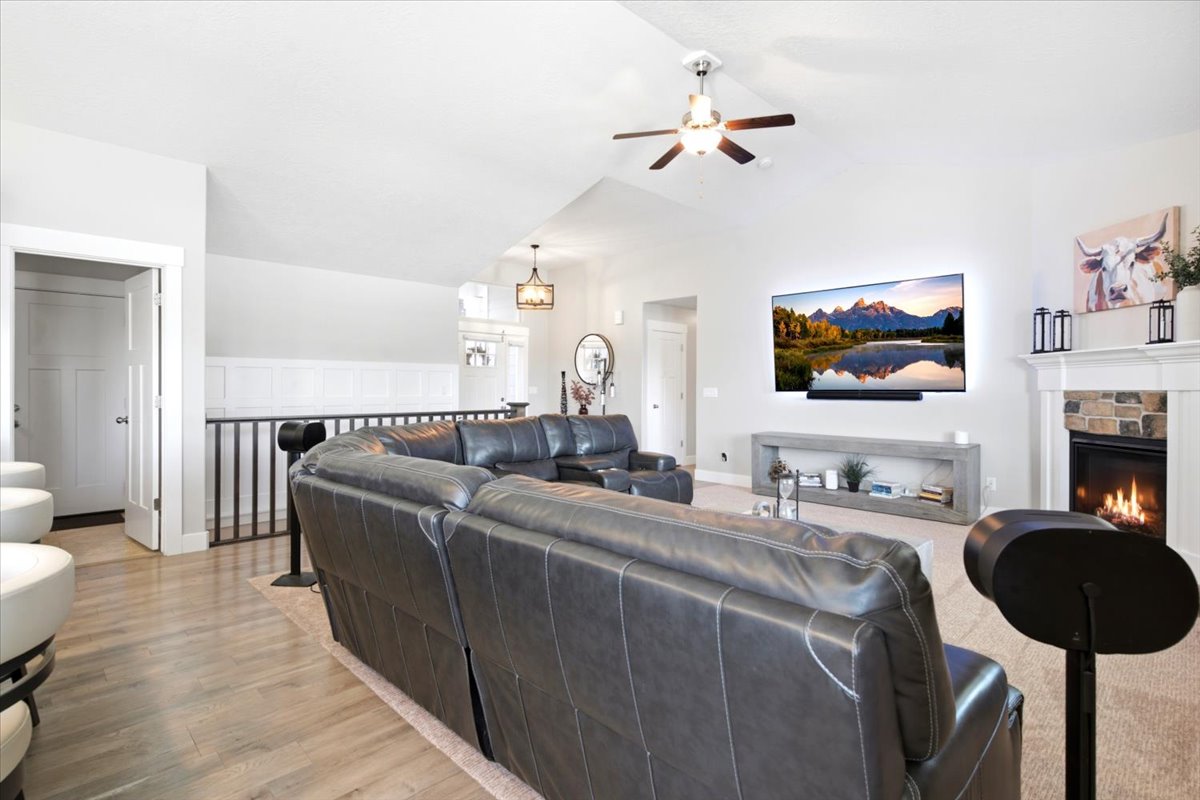 Spacious living area featuring a vaulted ceiling with a ceiling fan, a stone-surround fireplace with a white mantel, and wood-finish flooring