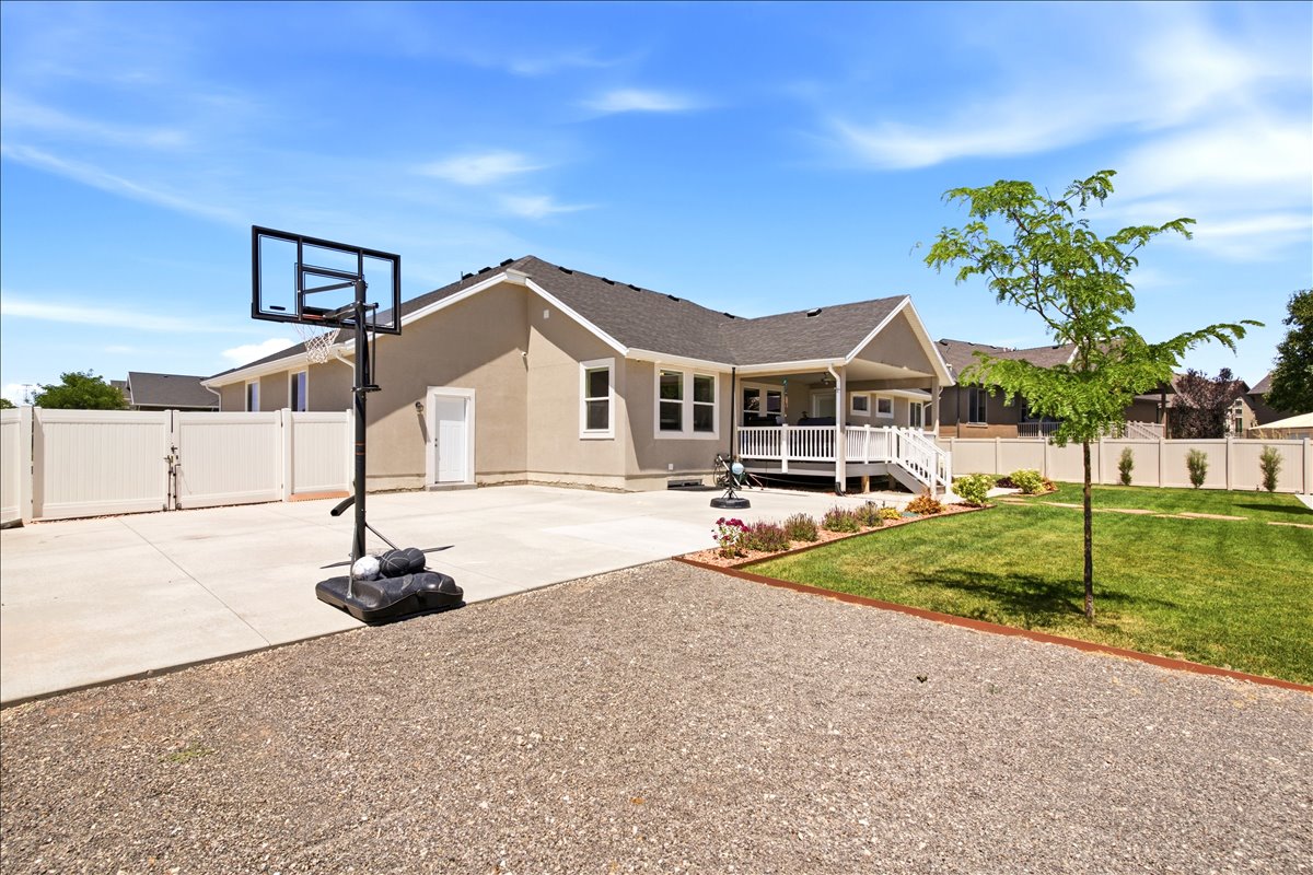 Expansive backyard featuring a covered patio, manicured lawn, gravel area, and white privacy fencing