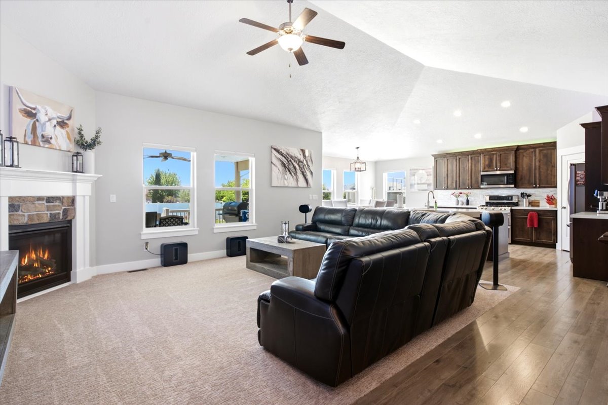 Spacious living area featuring vaulted ceilings, a stone-faced fireplace with a white mantel, and light carpeting