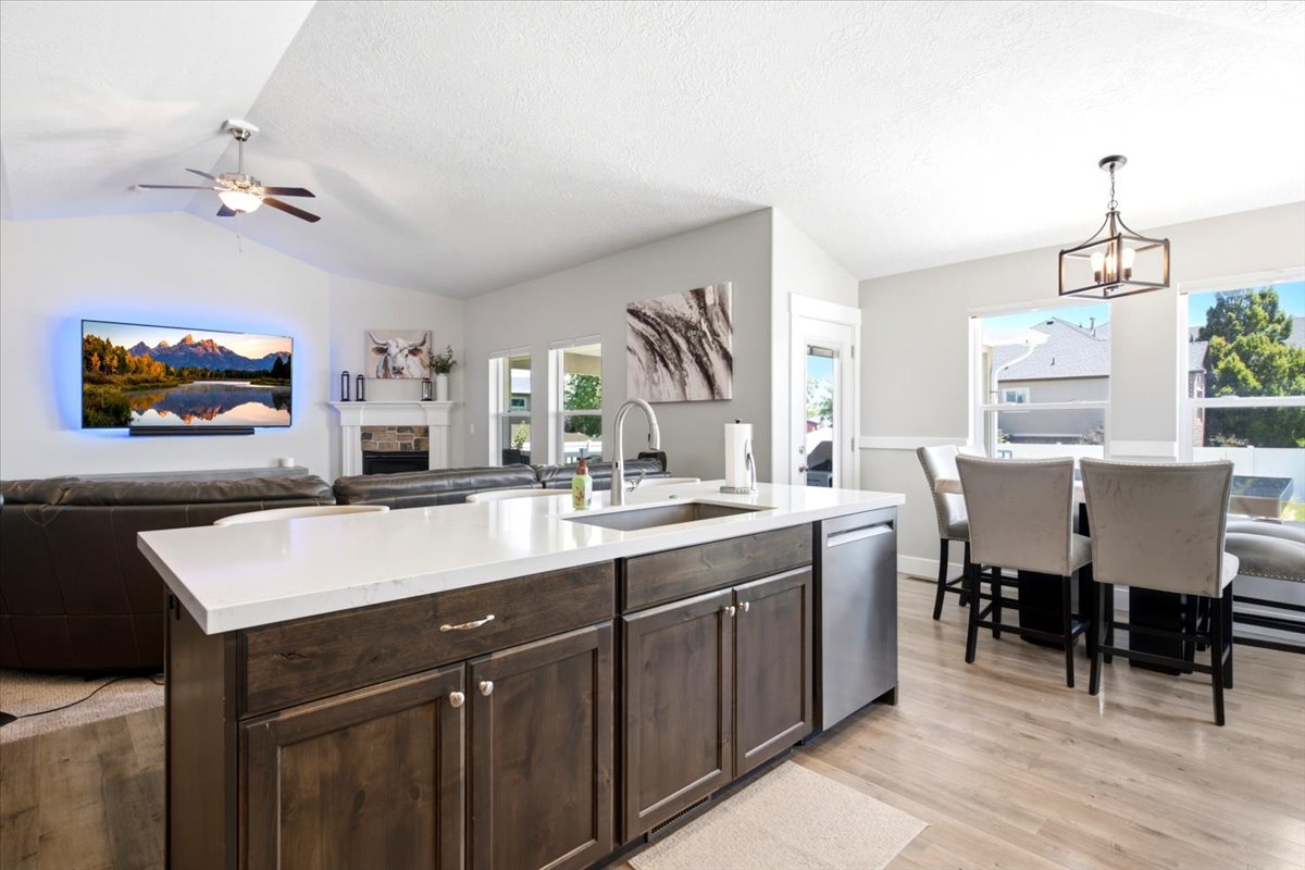 Kitchen island with white countertop and integrated sink, dark wood-finish cabinetry, and stainless steel dishwasher