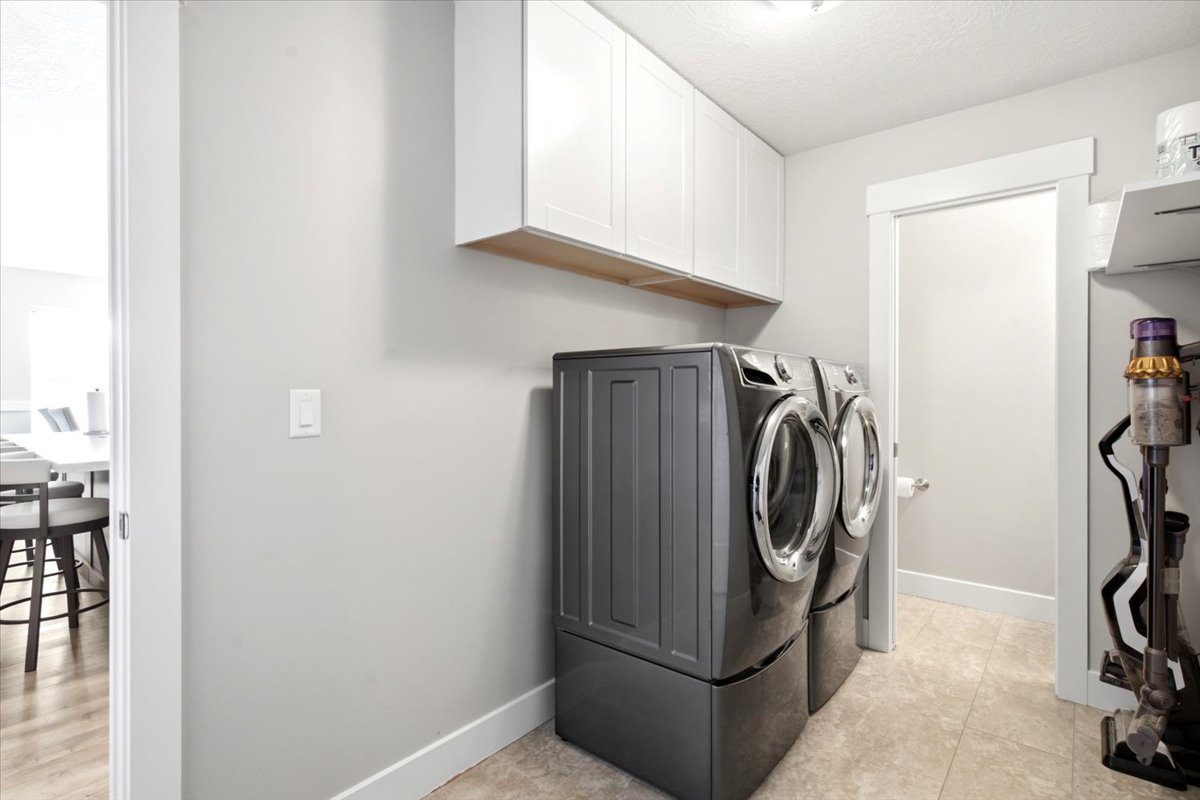 Dedicated laundry area featuring light gray walls, white baseboards, and white overhead cabinetry with a wood-finish underside