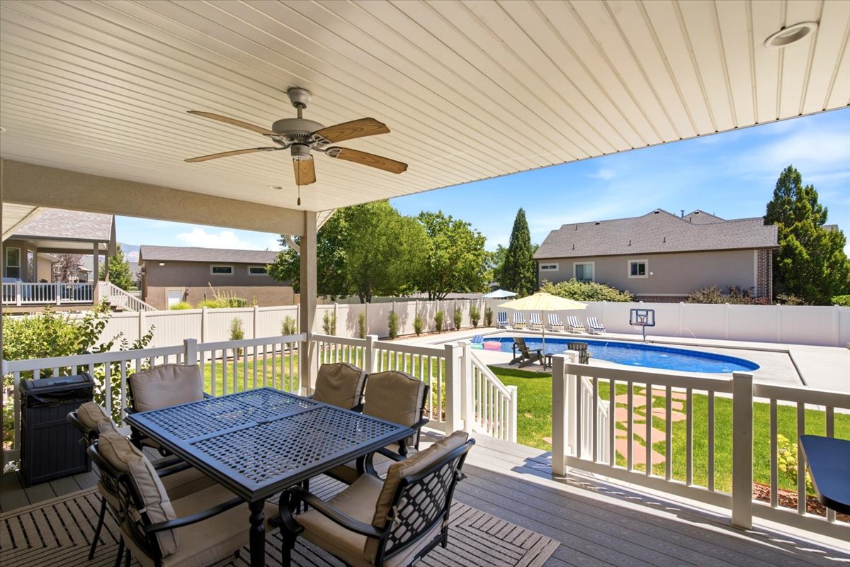 Expansive outdoor living area featuring a covered deck with a ceiling fan, composite decking, and white railings